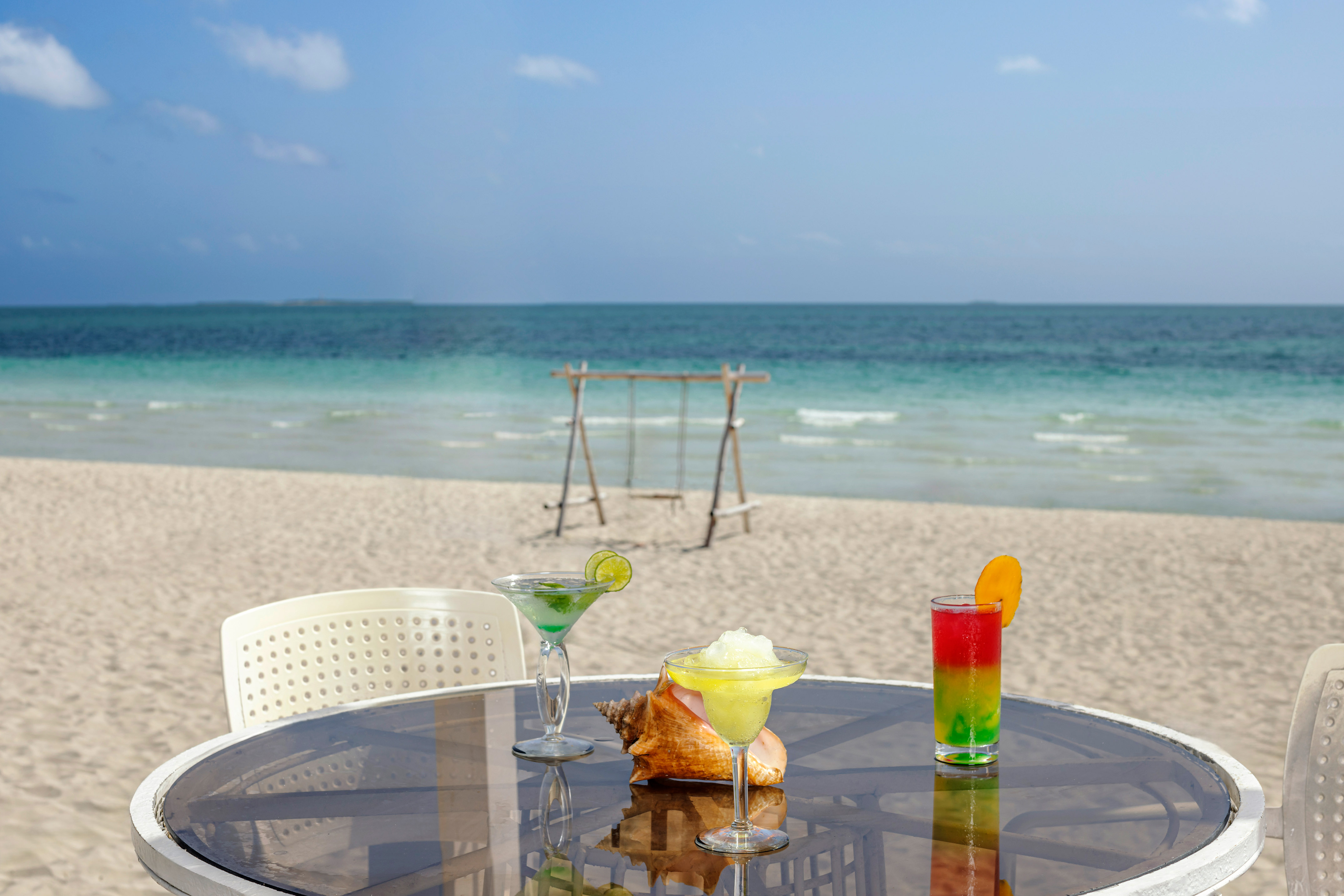 a table with drinks on it and a swing on the beach
