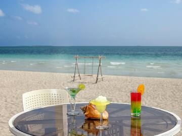 a table with drinks on it and a swing on the beach