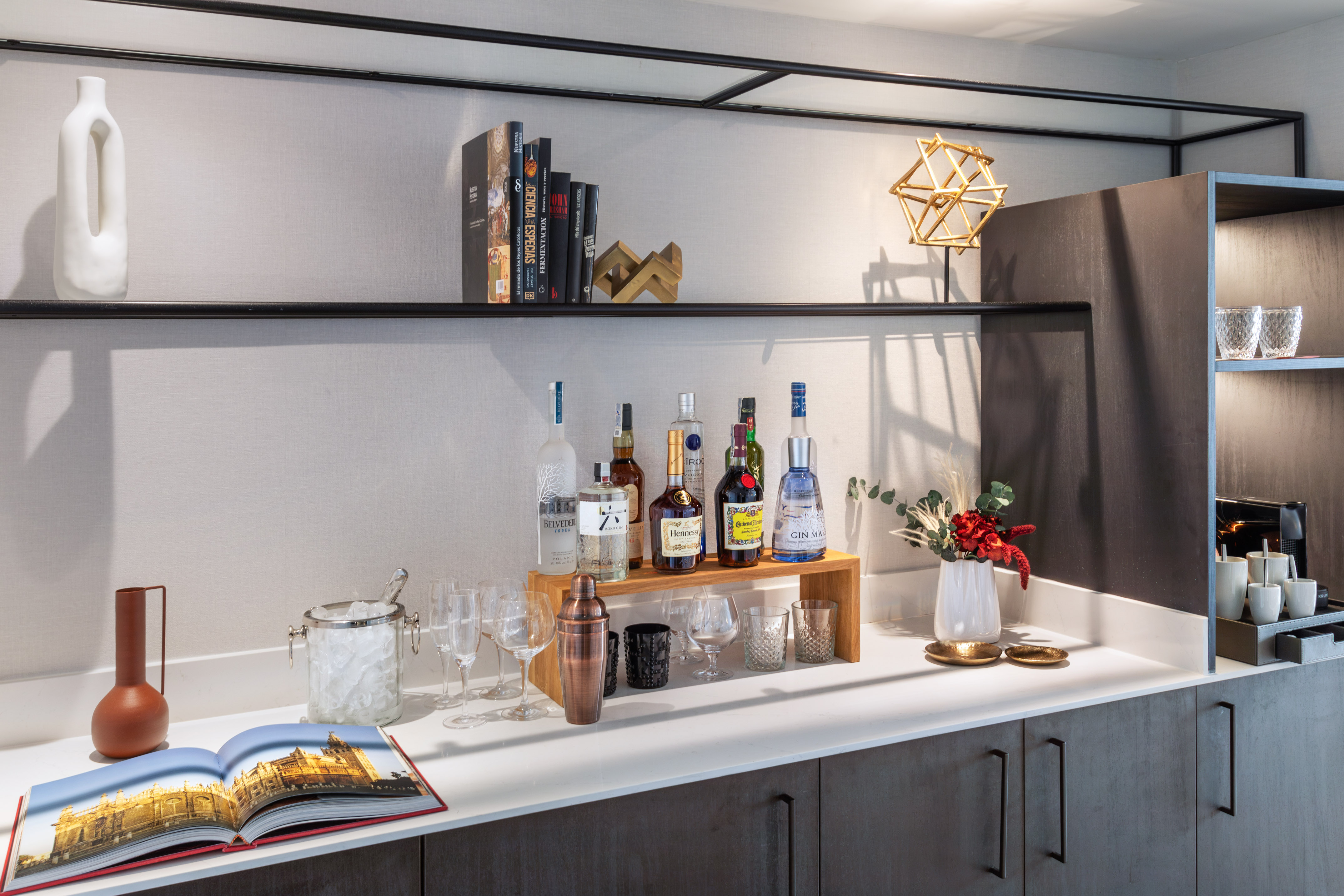 Hotel minibar with liquor bottles, cocktail glasses, bar tools on modern shelves.