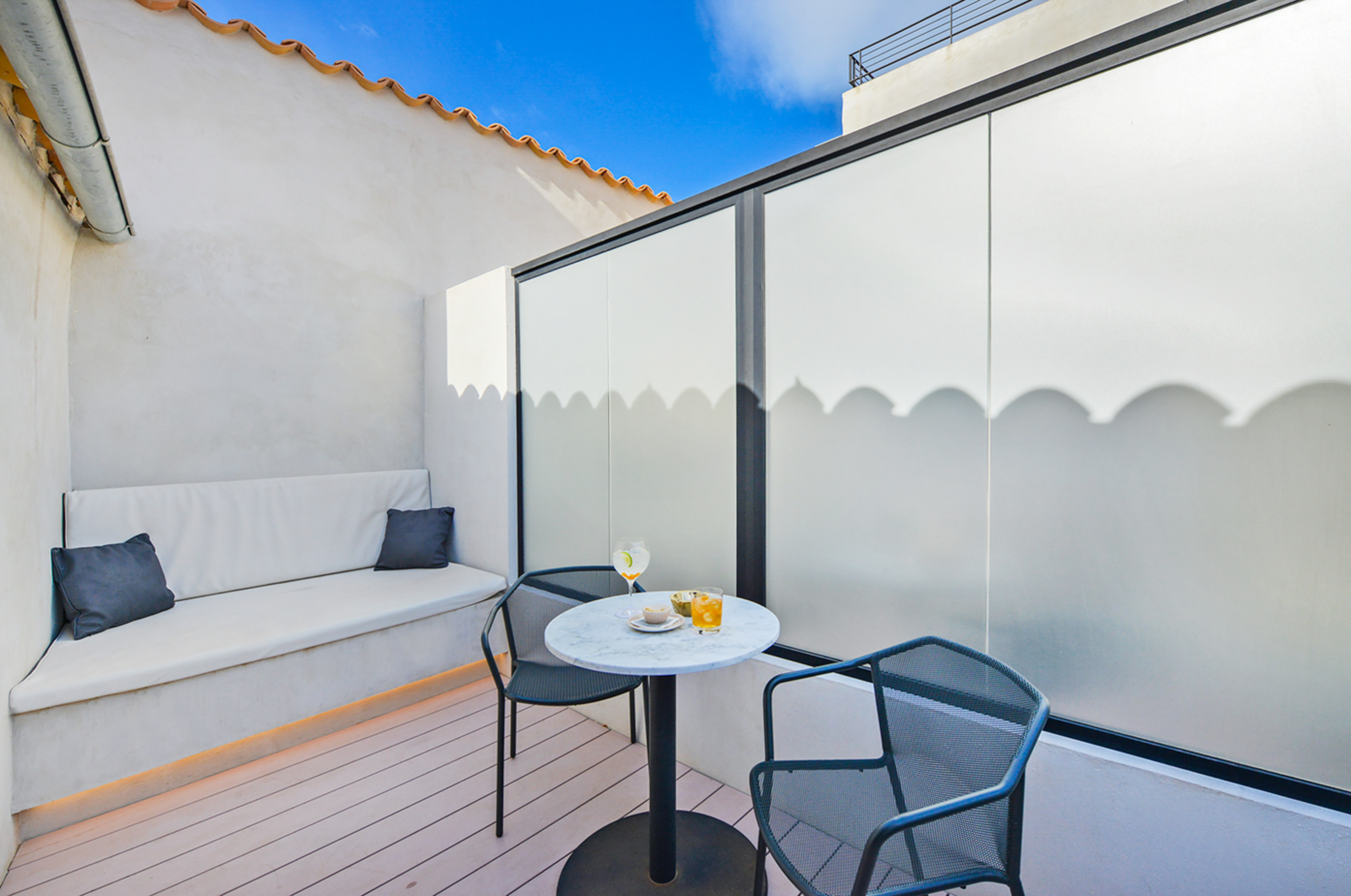 Modern outdoor patio with built-in bench, marble table, chairs, and drinks.