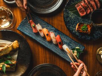 a person holding chopsticks over a plate of sushi