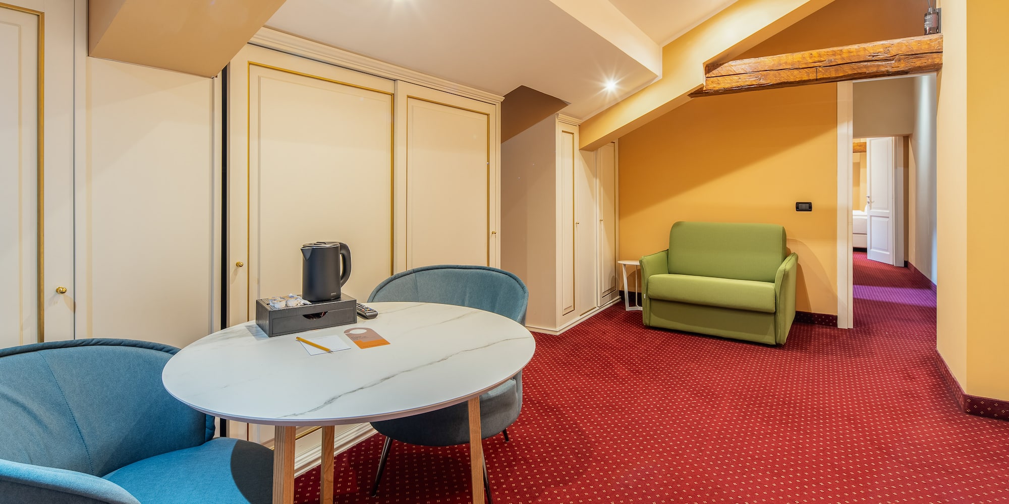 Hotel suite with red carpet, round table, blue chairs, and green sofa.
