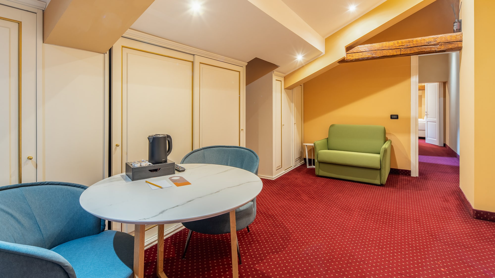Hotel suite with red carpet, round table, blue chairs, and green sofa.
