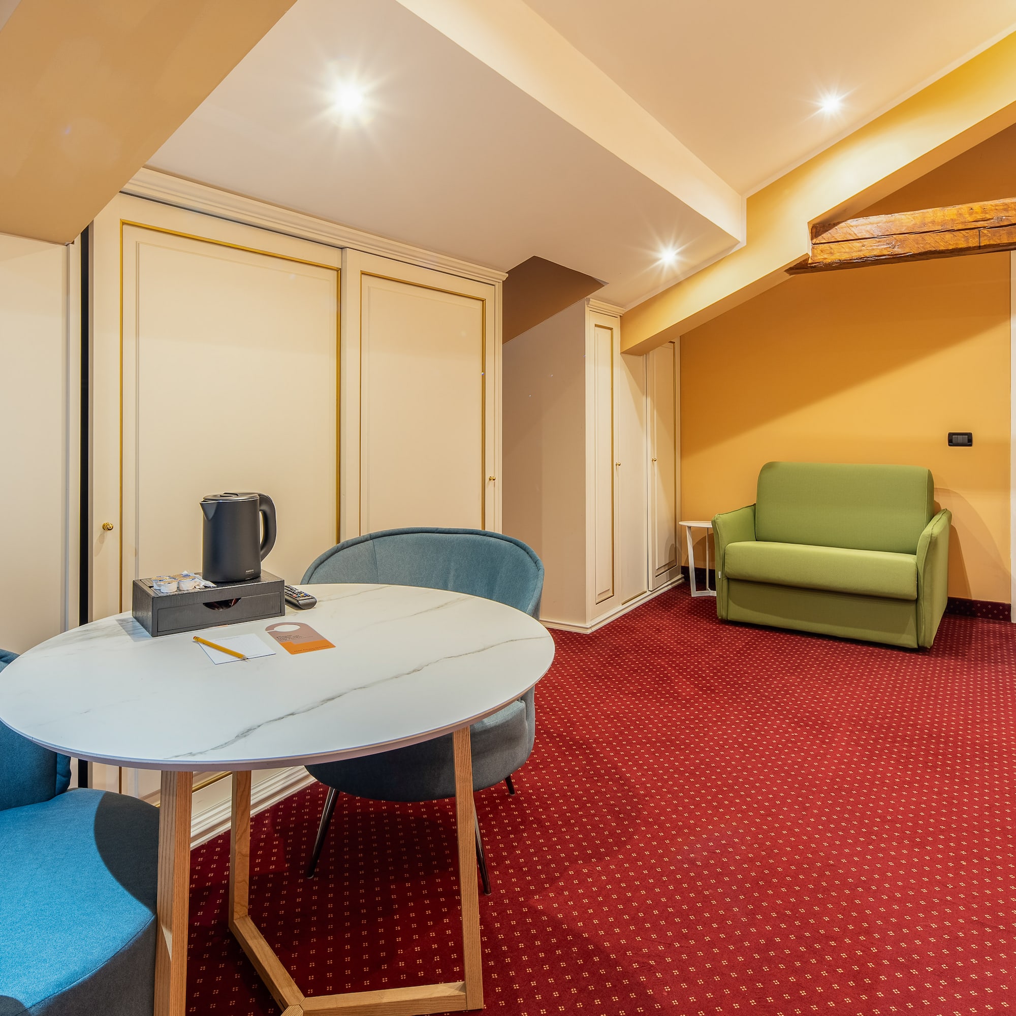 Hotel suite with red carpet, round table, blue chairs, and green sofa.