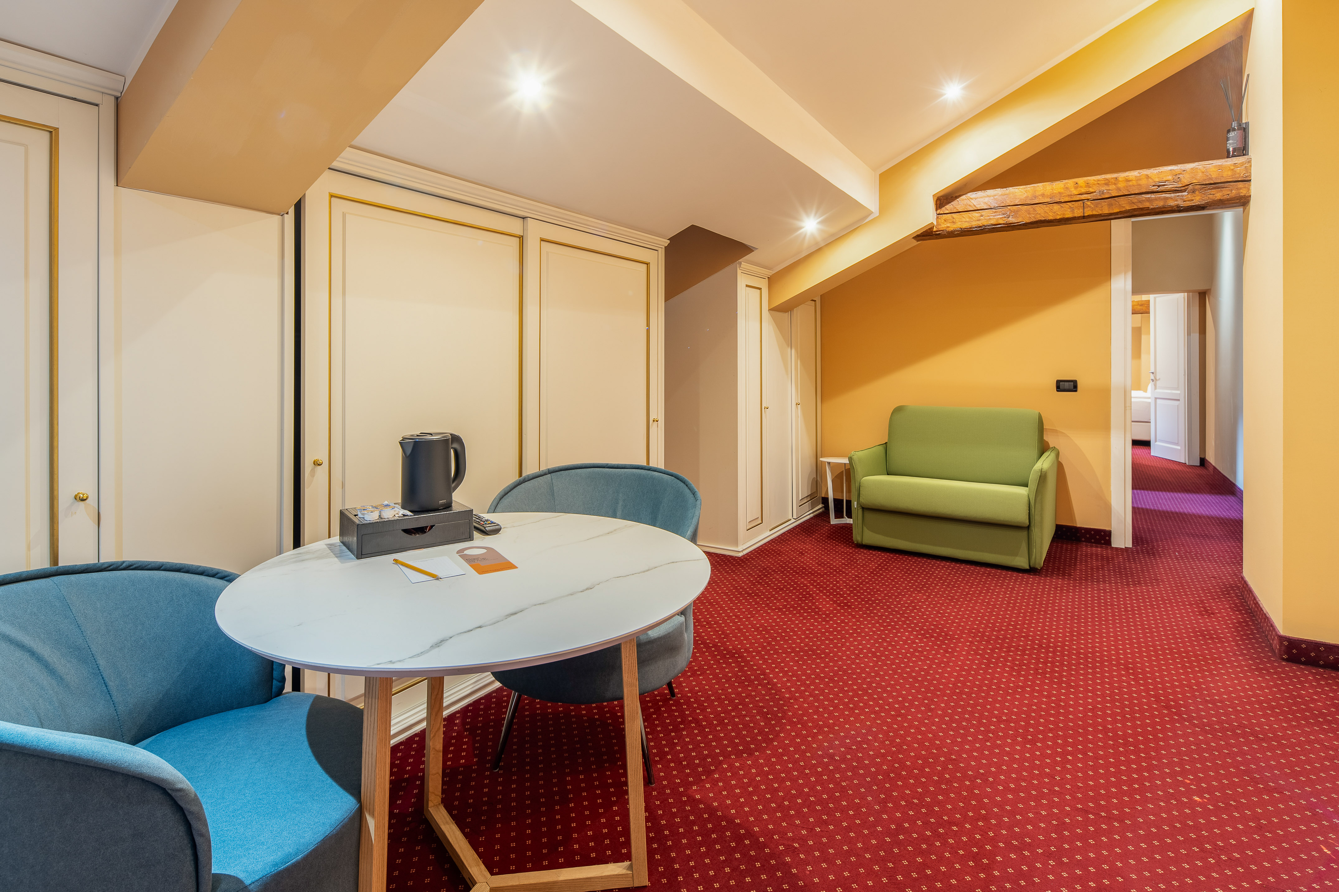 Hotel suite with red carpet, round table, blue chairs, and green sofa.
