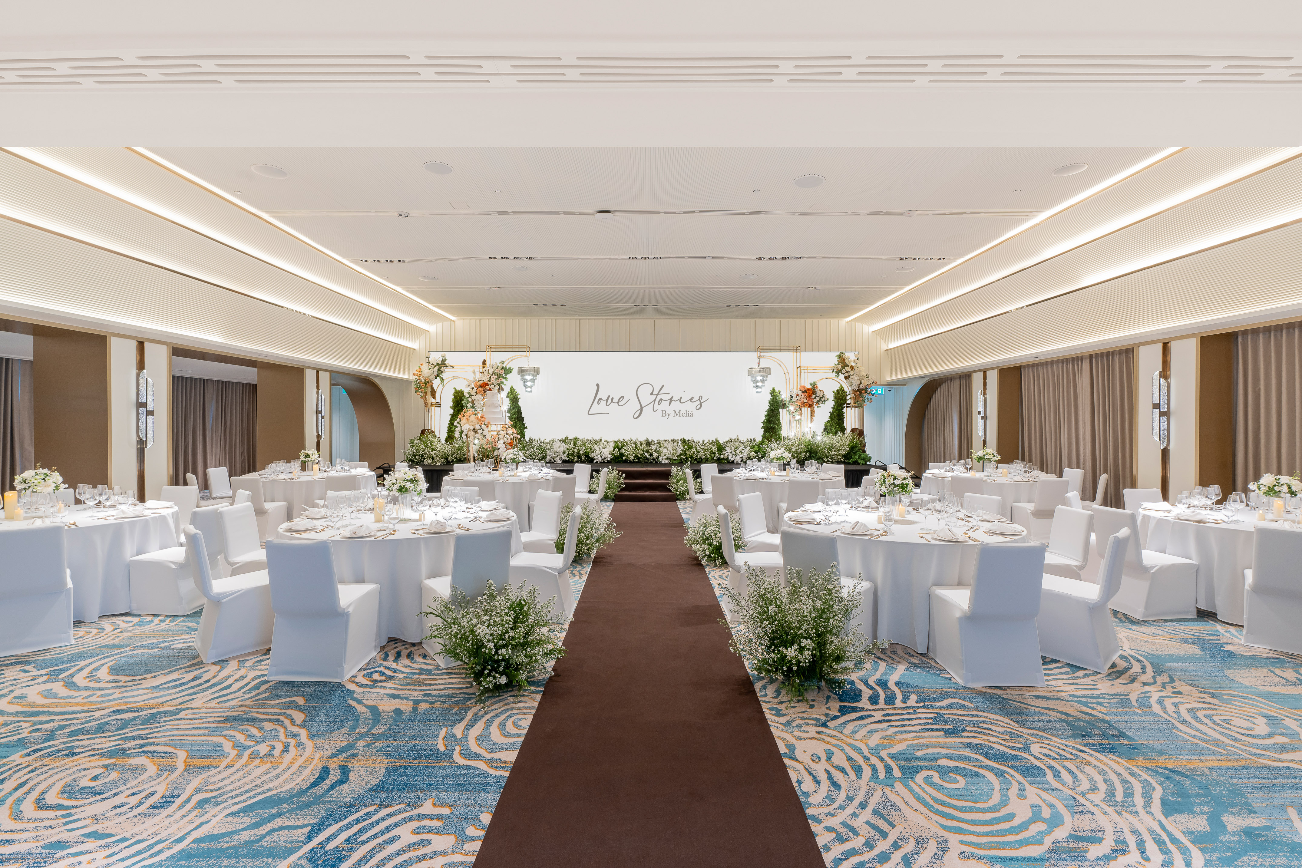 Elegant wedding ballroom, 'Love Stories' stage, white tables, floral decor.