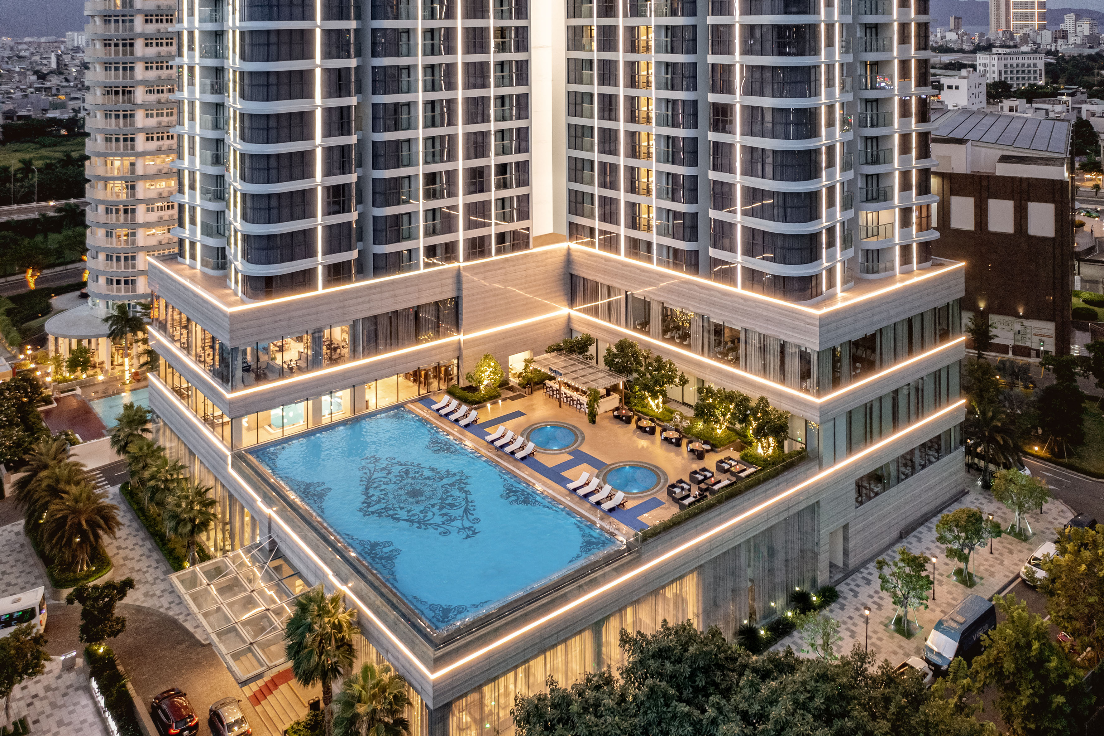 Luxury hotel rooftop pool and illuminated high-rise building at dusk.
