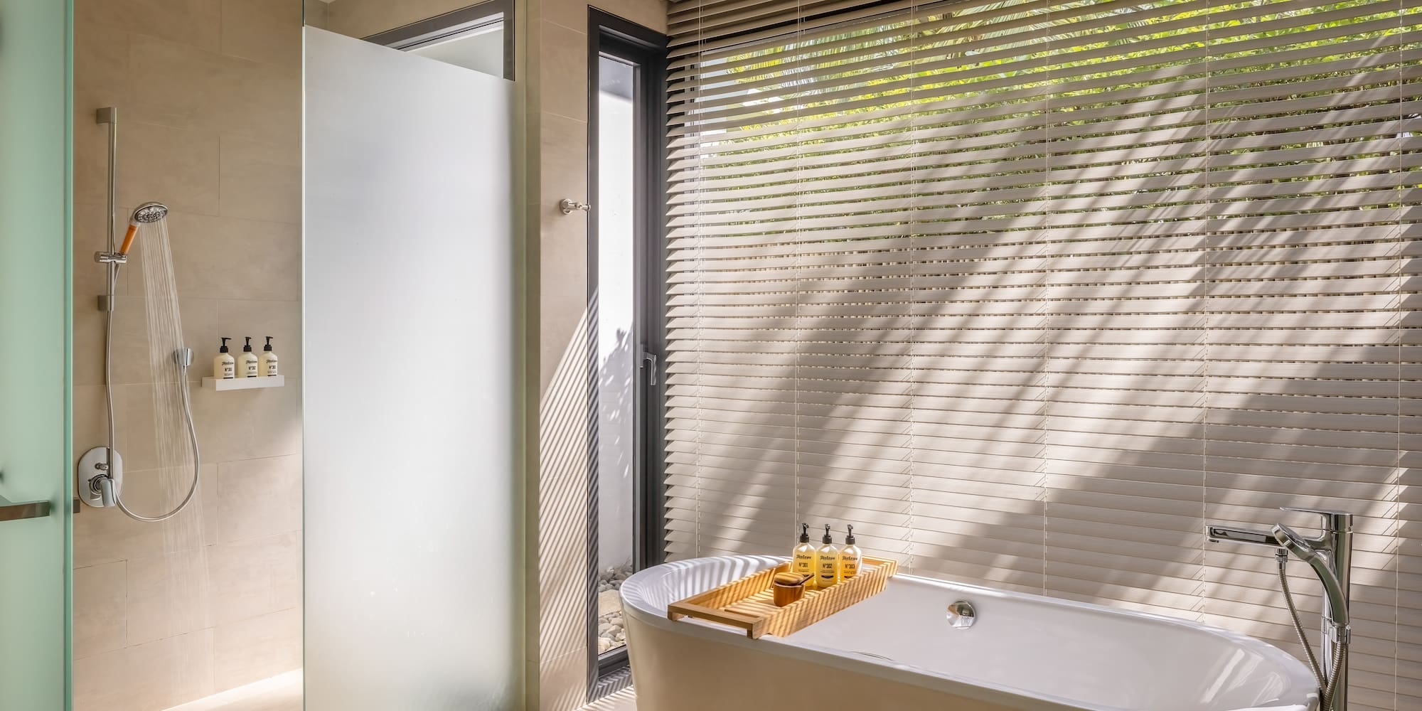Modern bathroom with freestanding bathtub, walk-in shower, and sunlit window blinds.