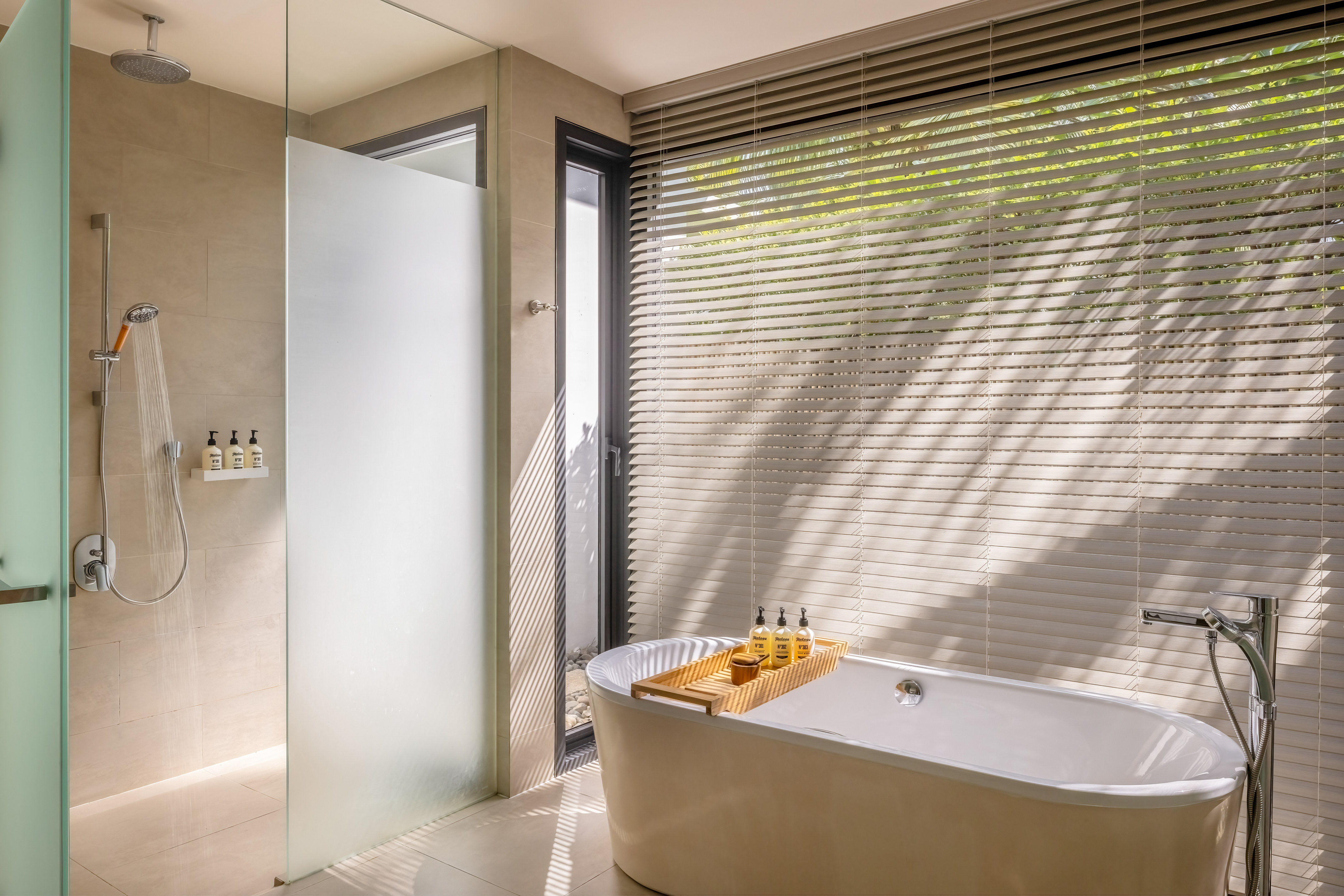 Modern bathroom with freestanding bathtub, walk-in shower, and sunlit window blinds.