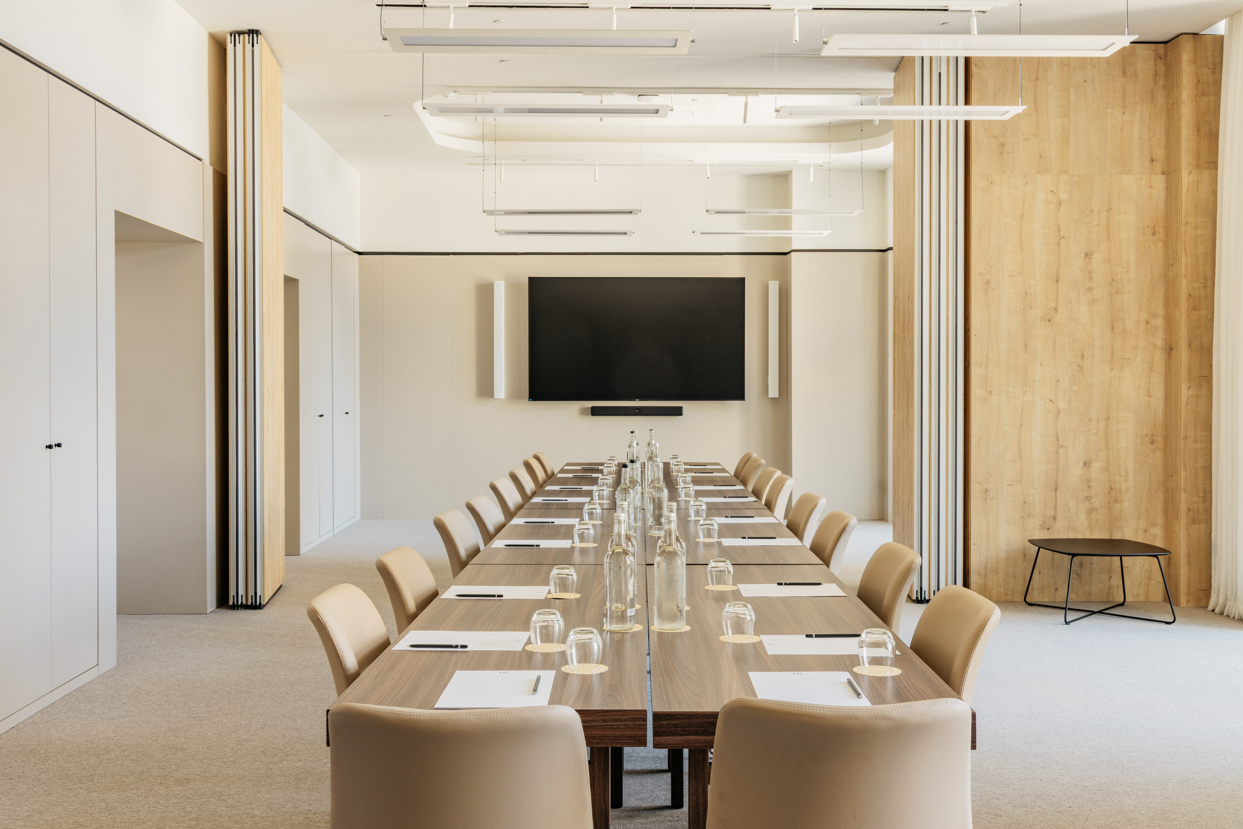 Modern conference room with long table, beige chairs, and wall screen.