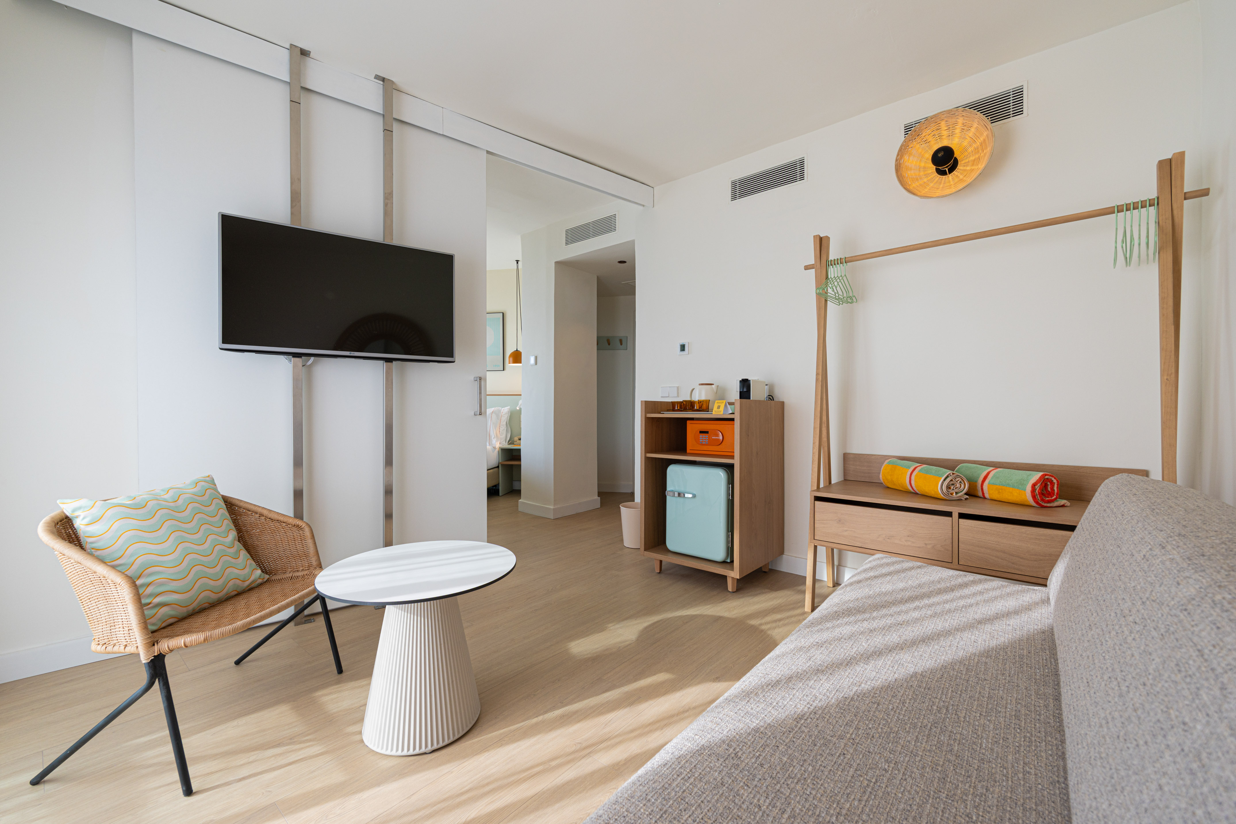 Modern hotel room with flat-screen TV, rattan chair, and wooden furniture.