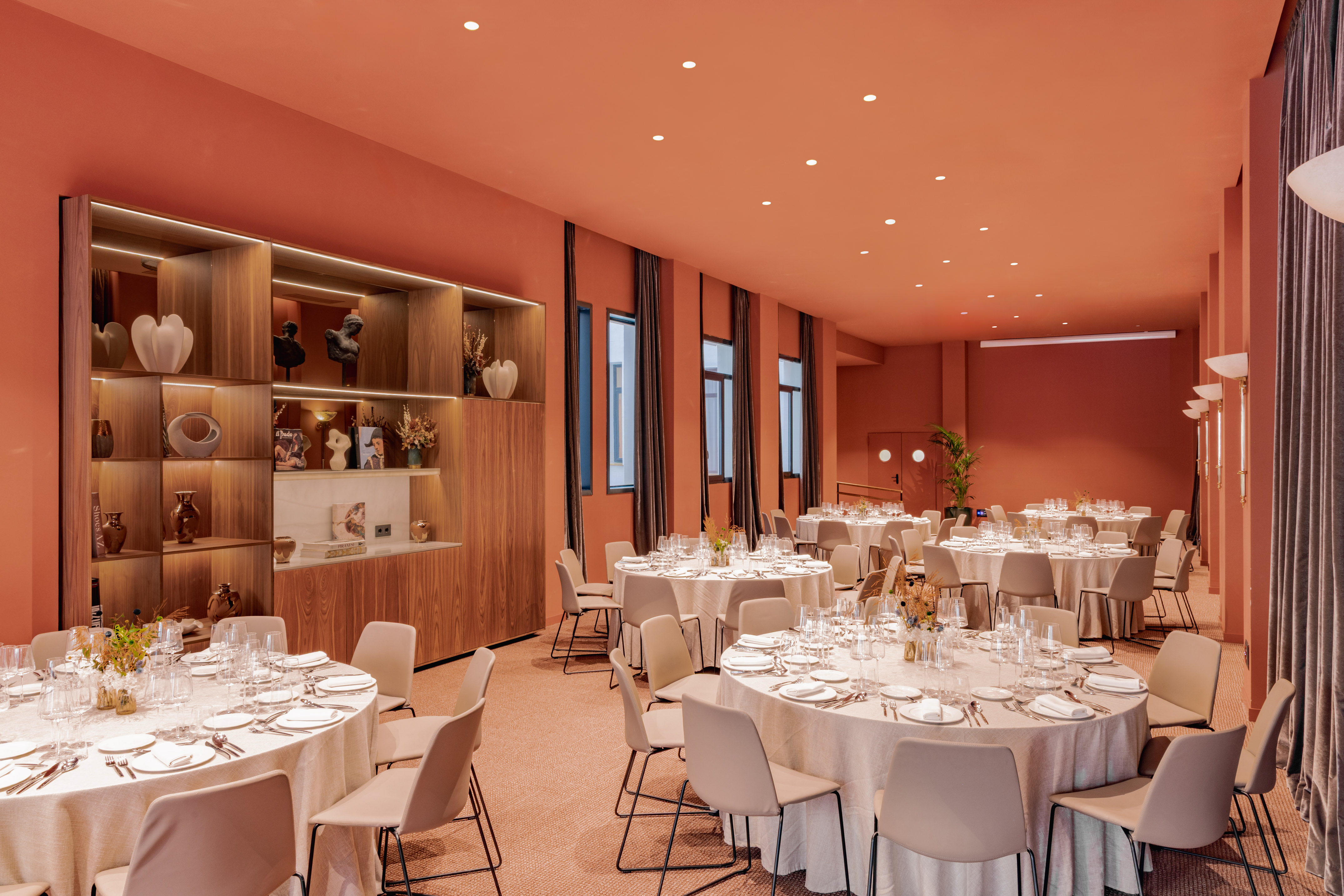 Elegant event space with round dining tables, terracotta walls, and modern decor.