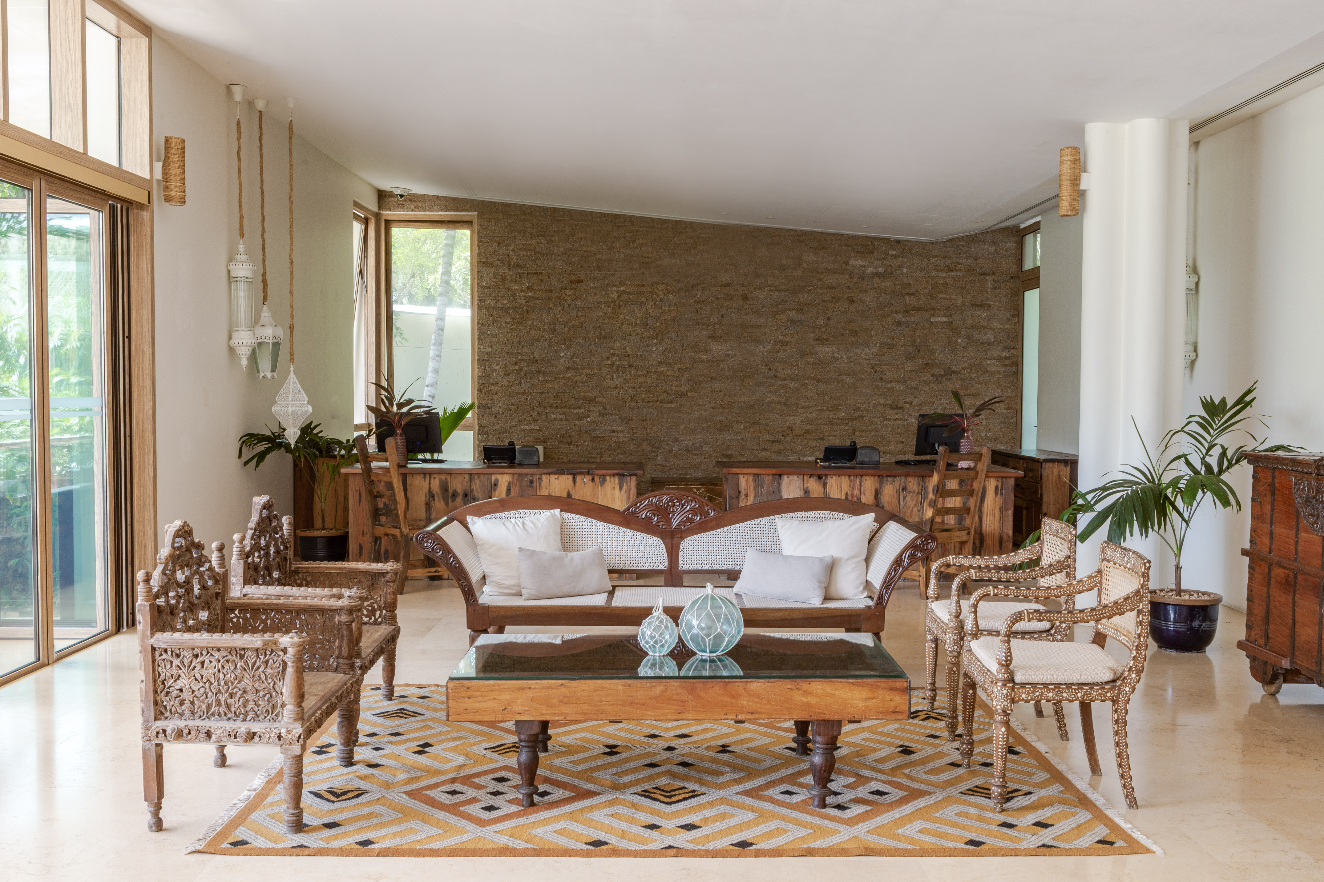 Hotel lobby with carved wooden furniture, rattan sofa, and geometric rug.