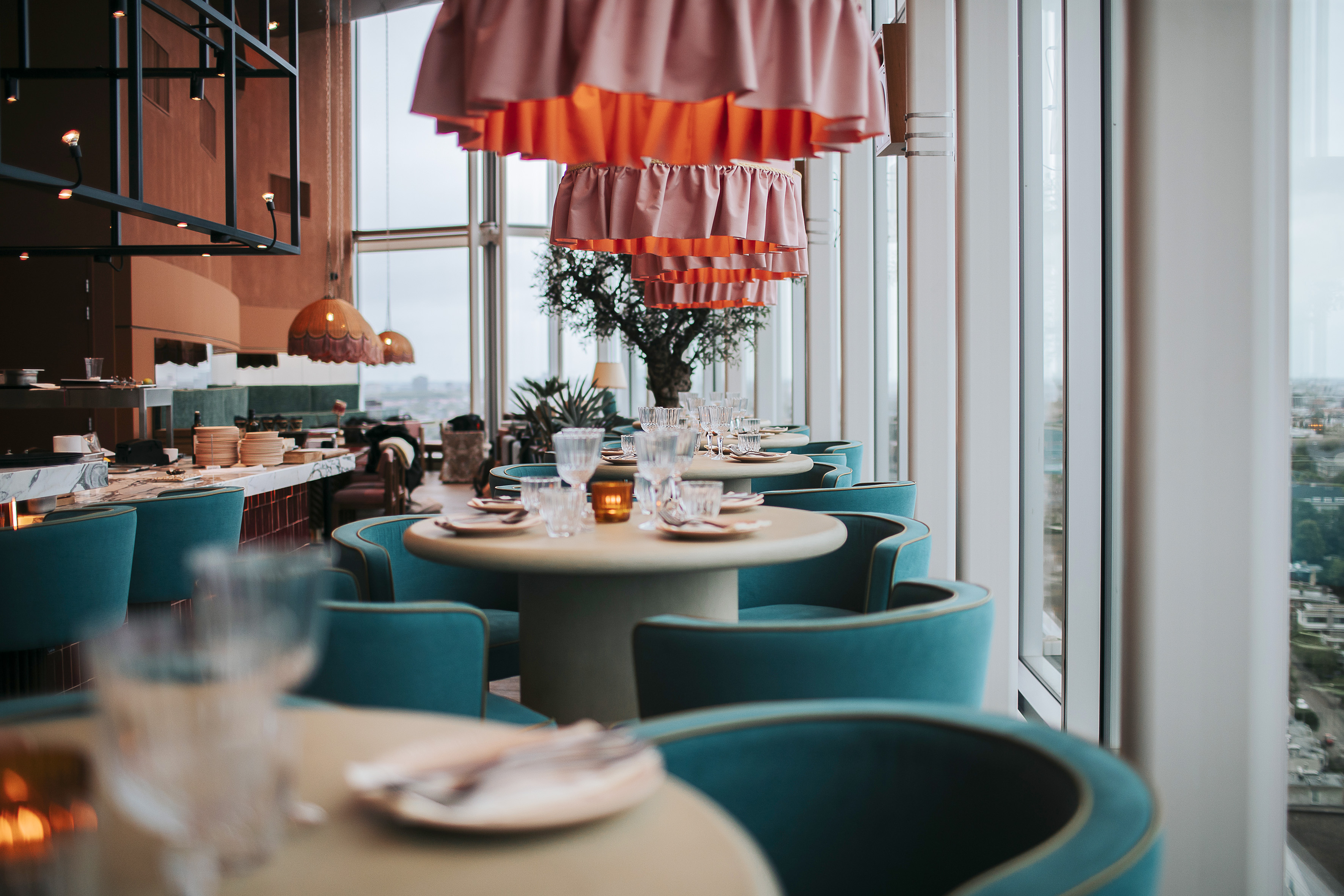 Elegant high-rise restaurant interior with pink lights and teal chairs.