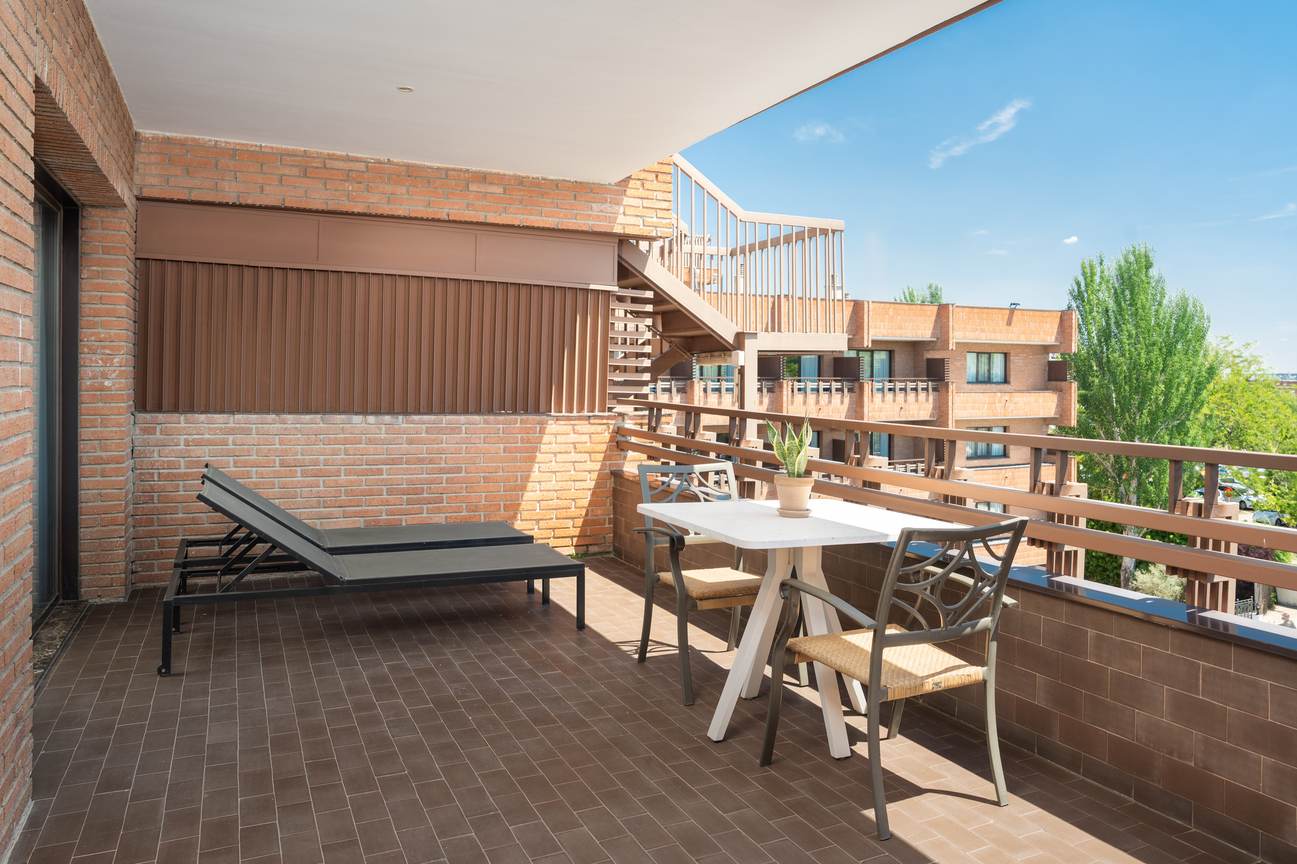 Sunny brick apartment balcony with lounge chair, outdoor table, and chairs.