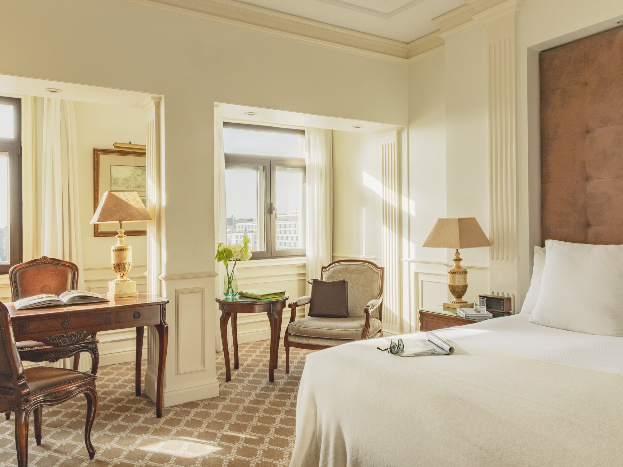 Luxurious hotel room with a large bed, elegant desk, and sunlit windows.