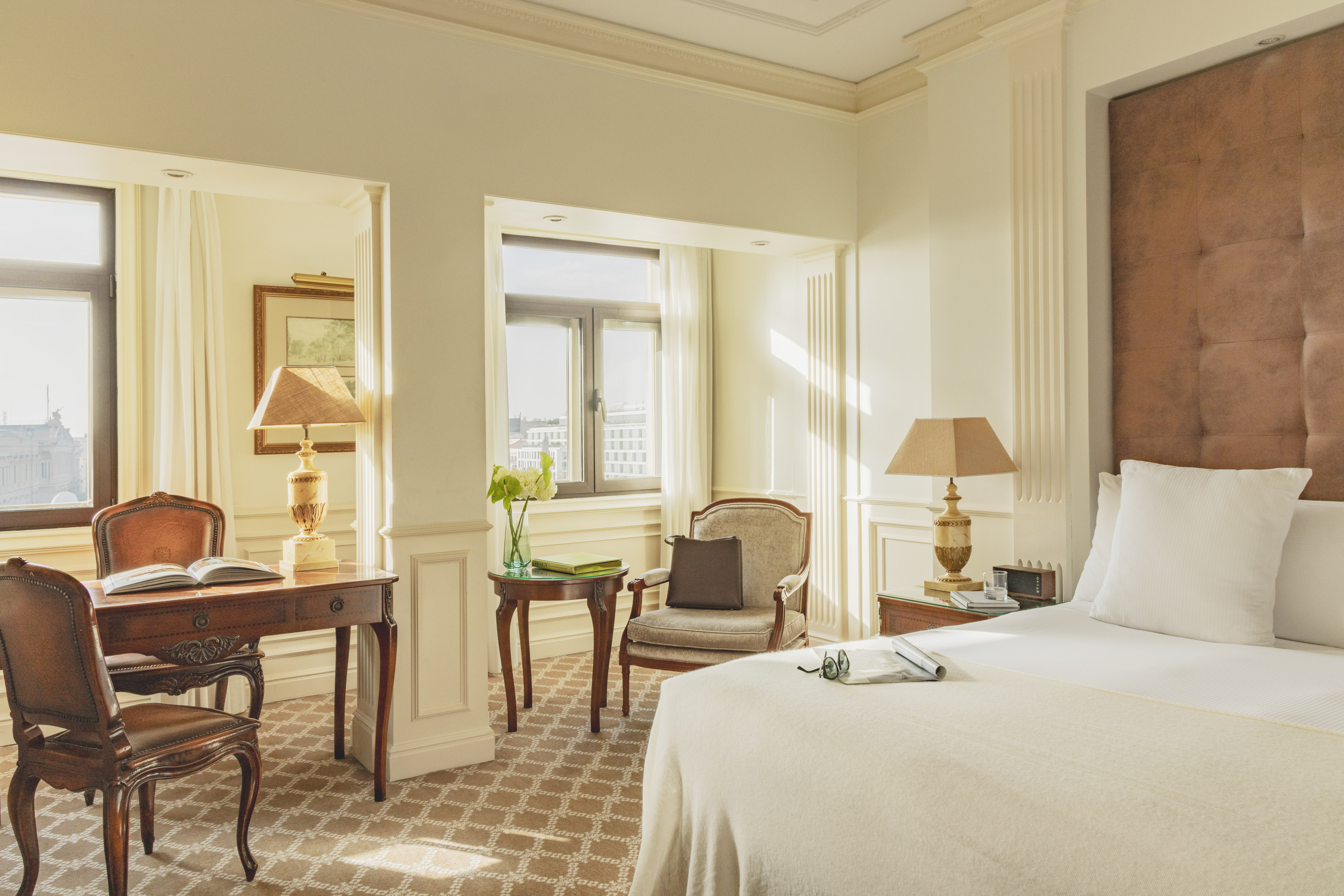 Luxurious hotel room with a large bed, elegant desk, and sunlit windows.