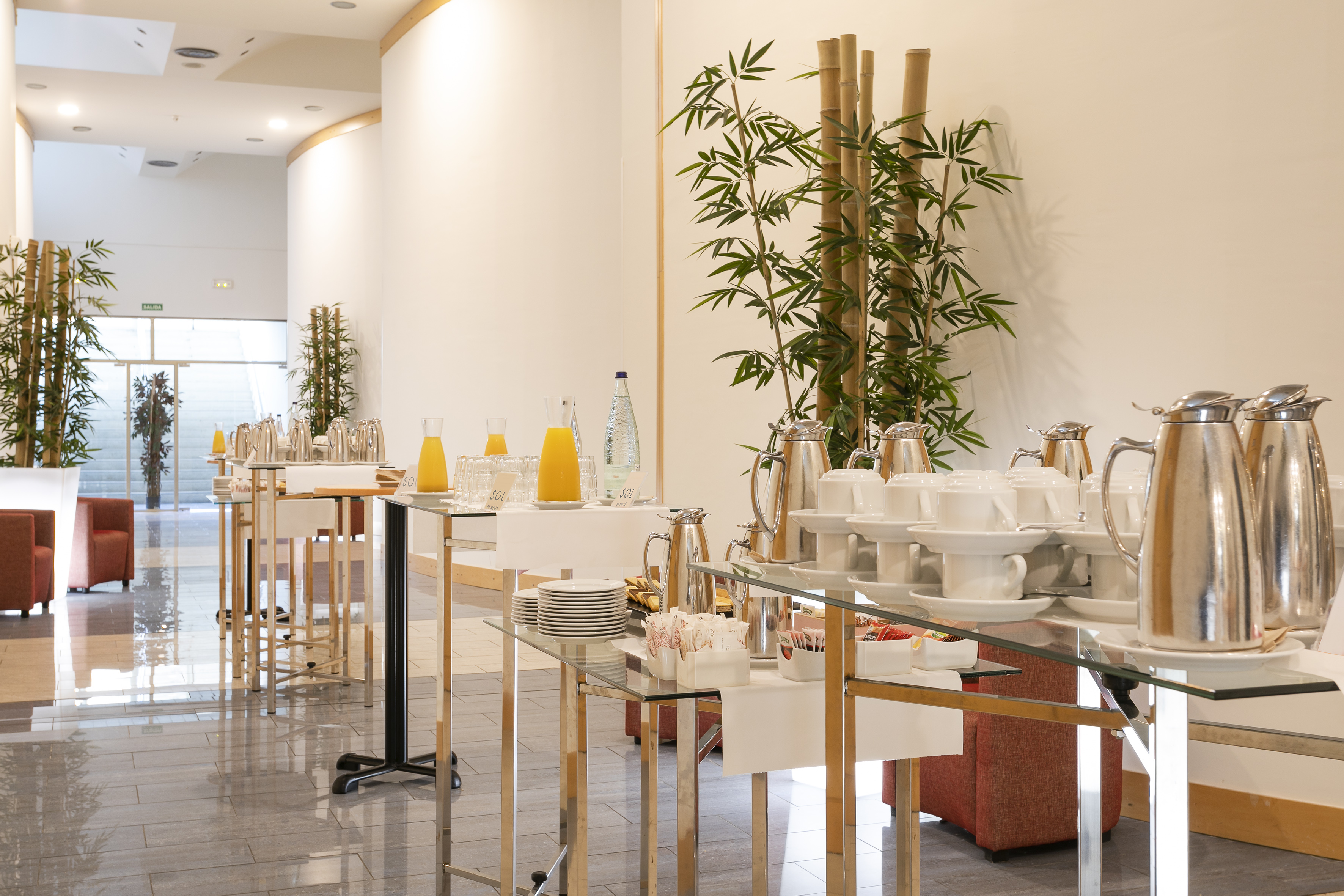 Hotel event refreshment station with coffee, juice, cups, and bamboo decor.