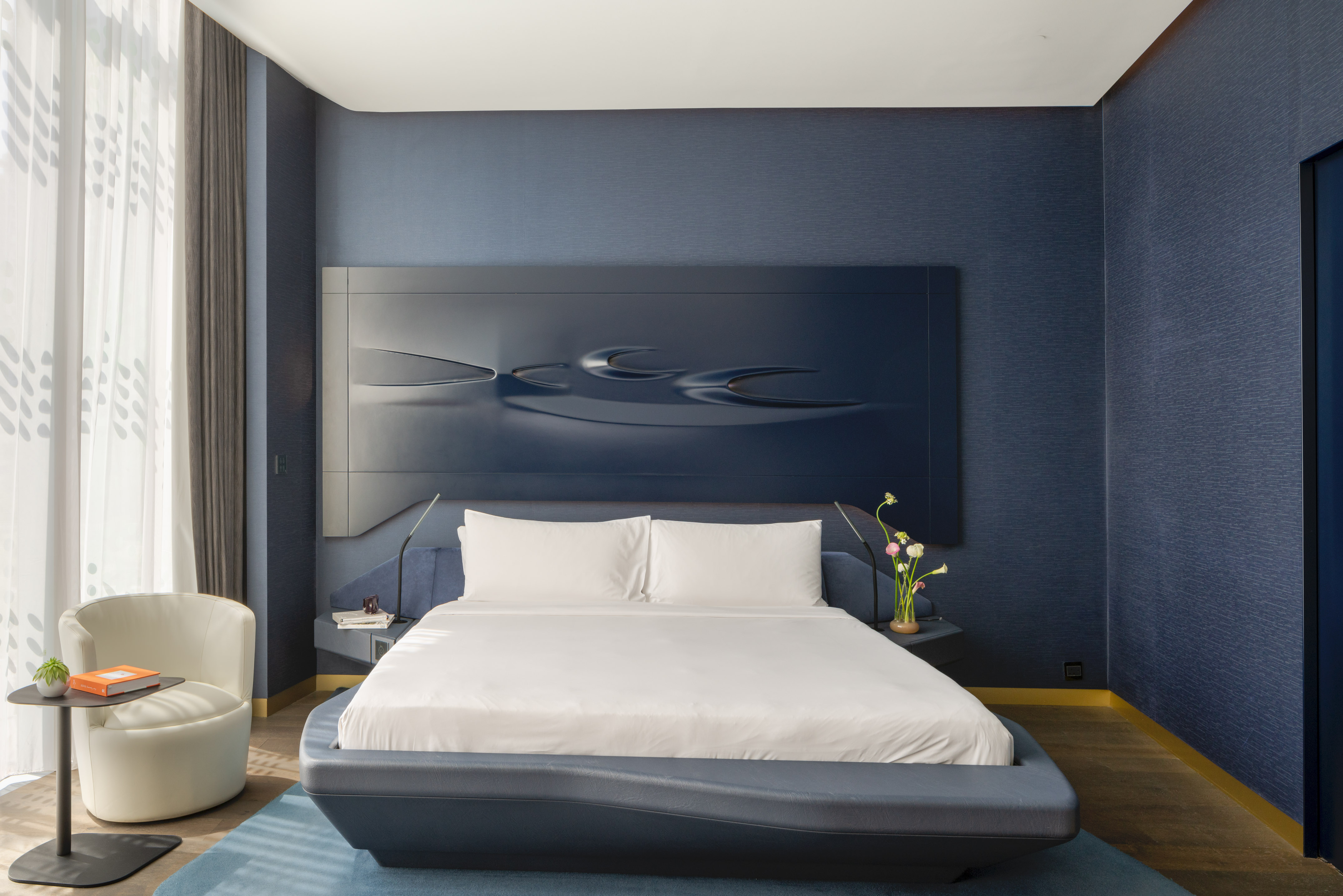 Modern hotel bedroom with navy blue sculptural headboard and white bed.