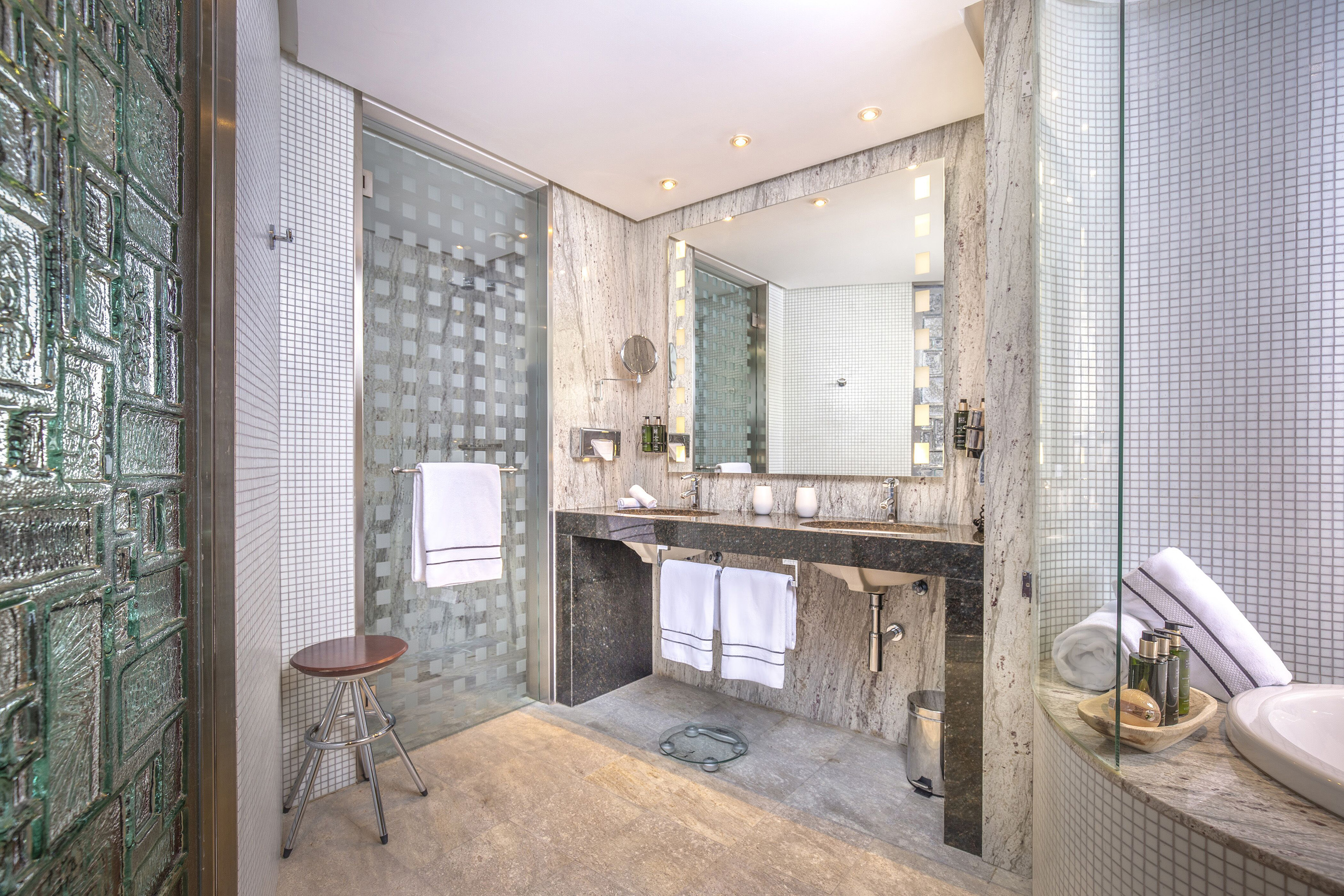 Contemporary bathroom with double vanity, granite, glass shower, and white mosaic tiles.