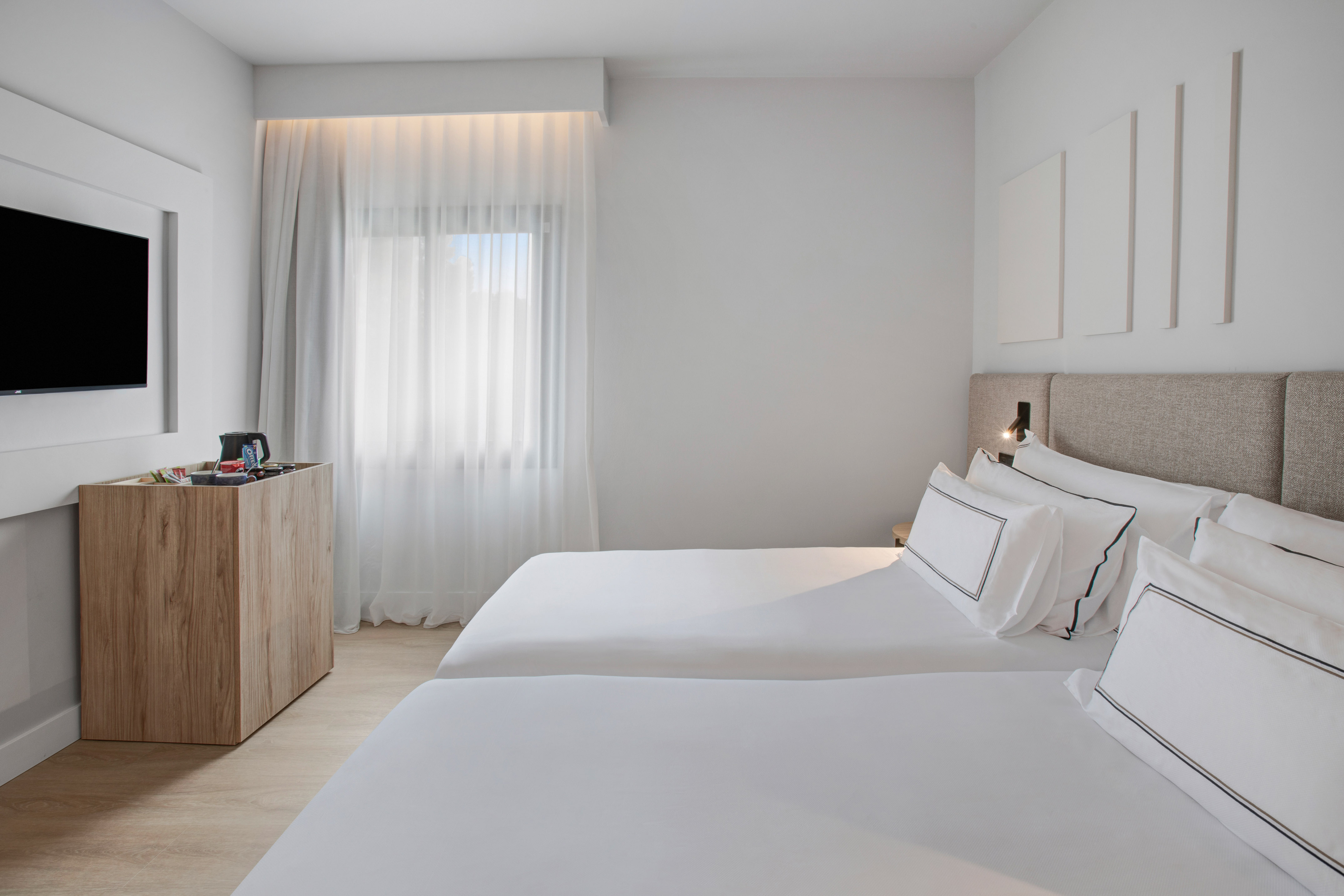 Modern hotel room with two single beds, white linens, TV, and large window.