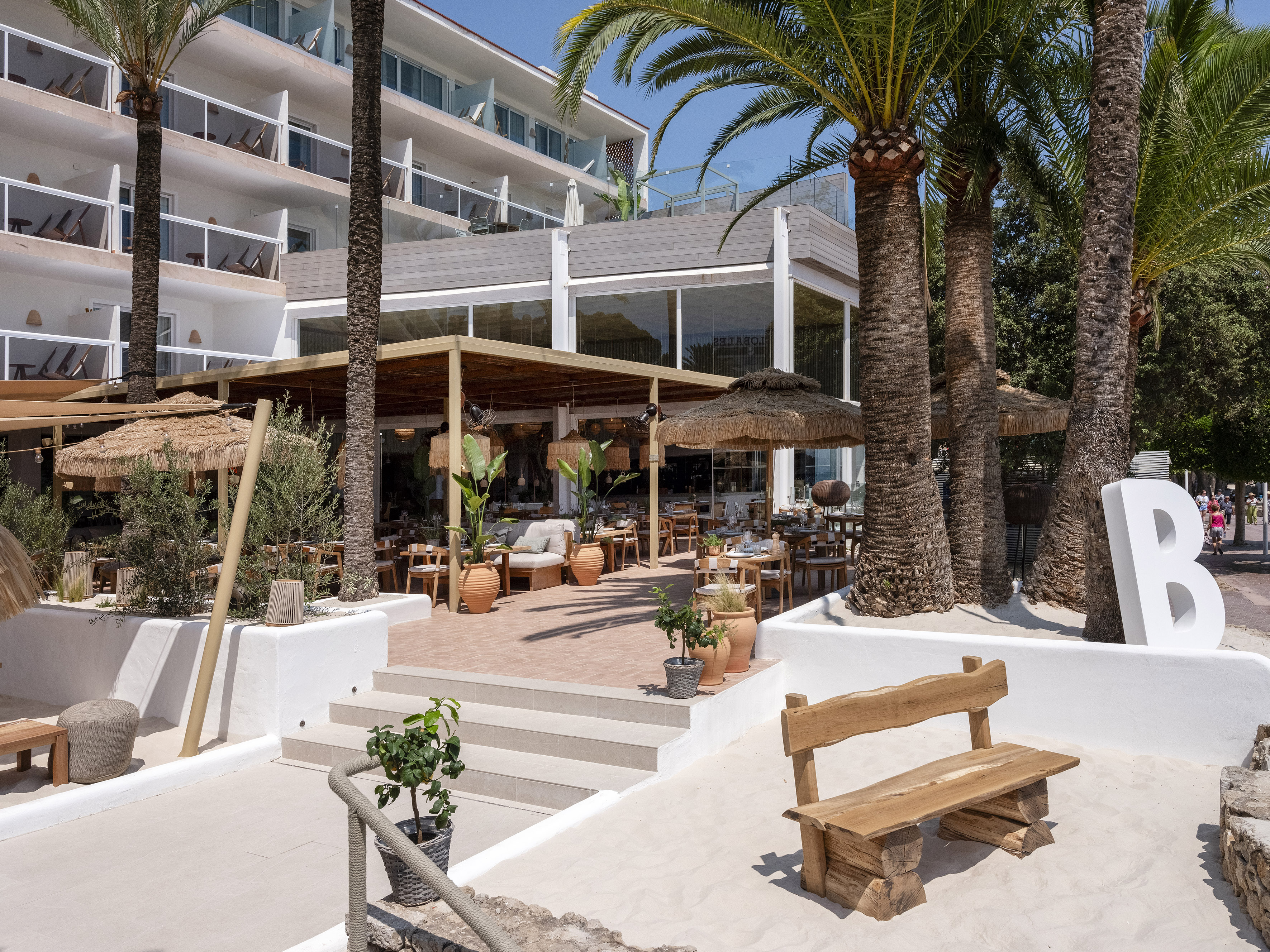 Tropical hotel terrace restaurant with palm trees and a sandy lounge.