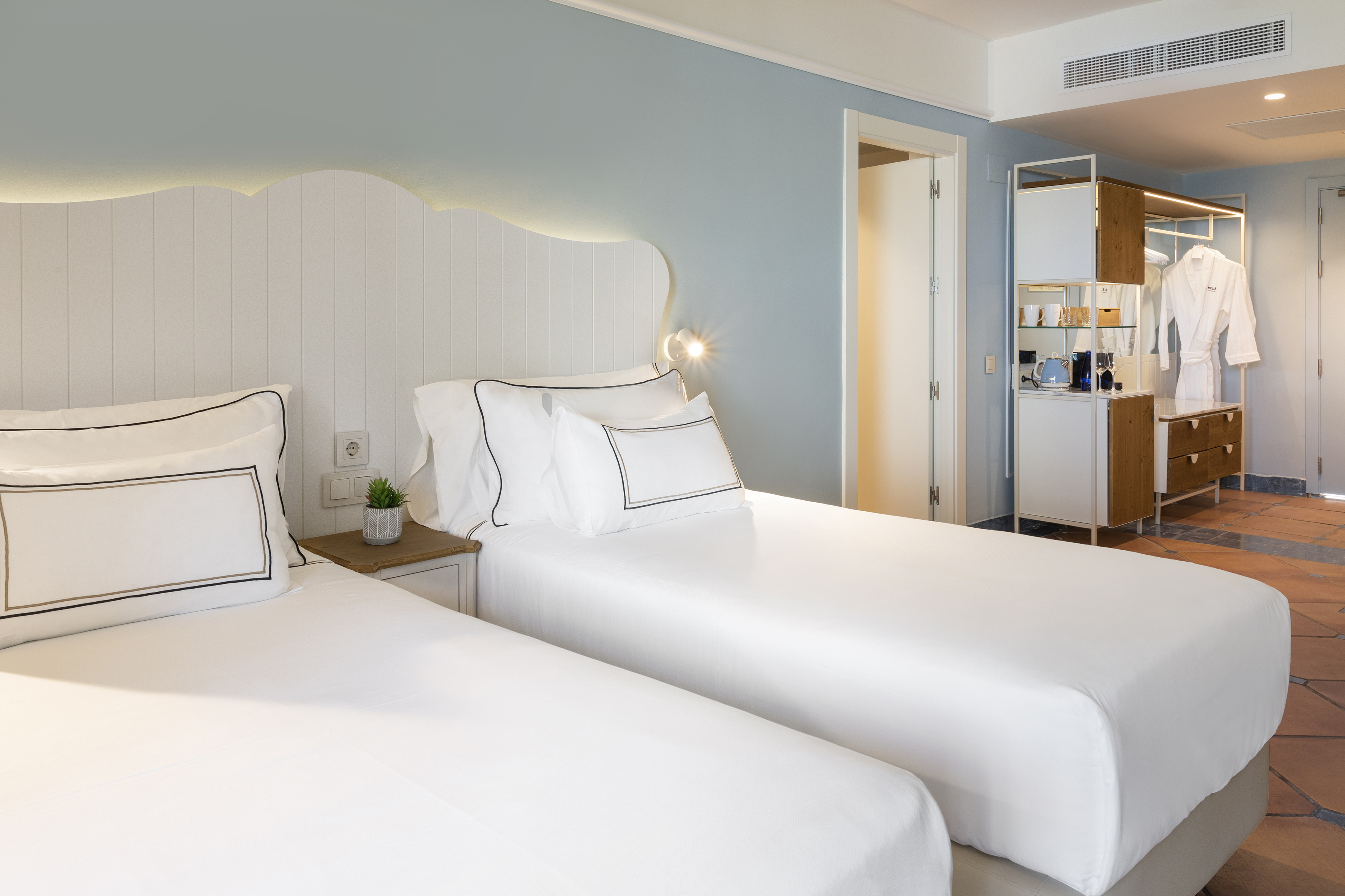 Modern hotel room with two twin beds, white linens, and built-in wardrobe.