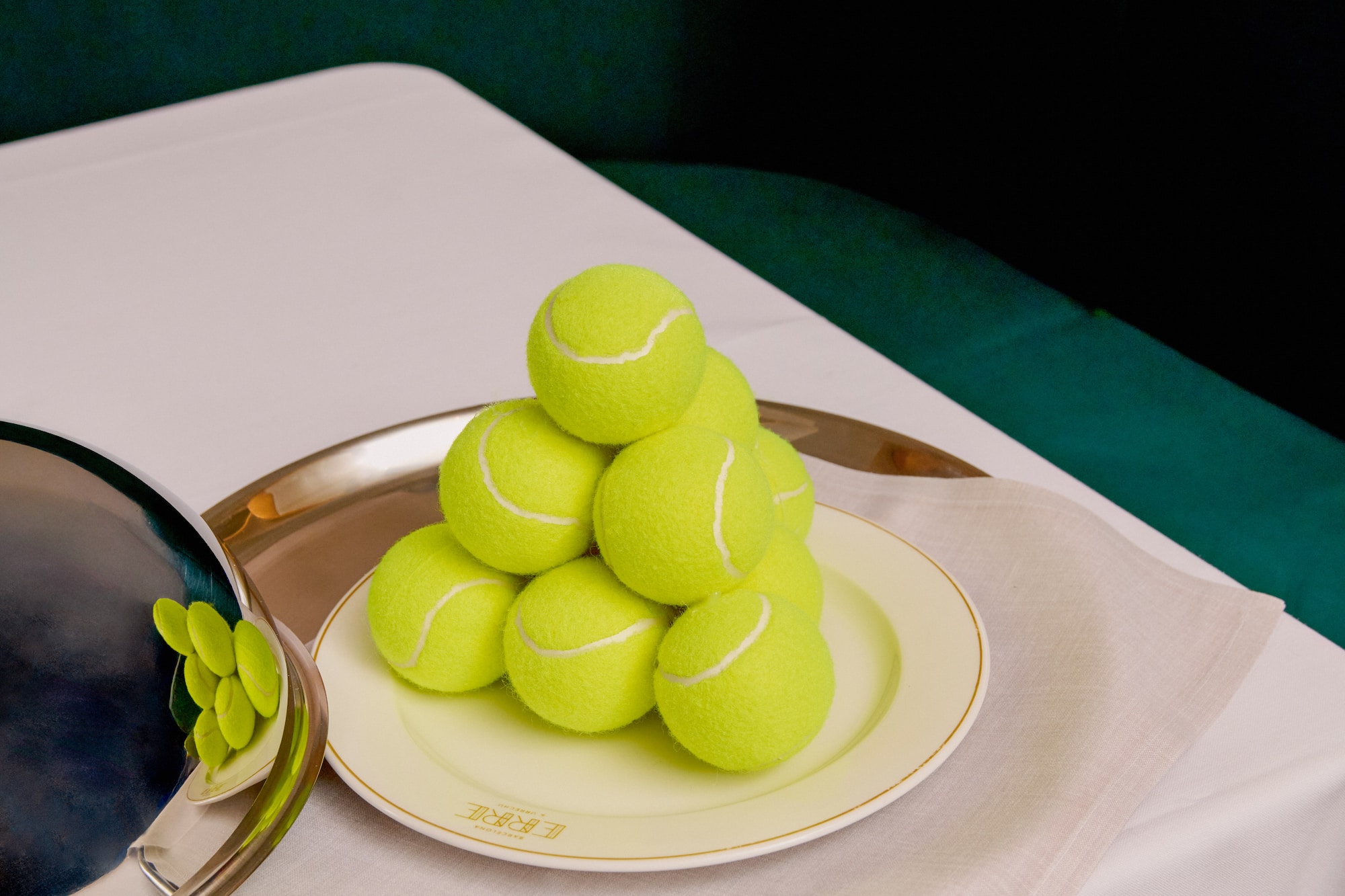 Pyramid of vibrant tennis balls on a luxury plate with silver cloche and tray.