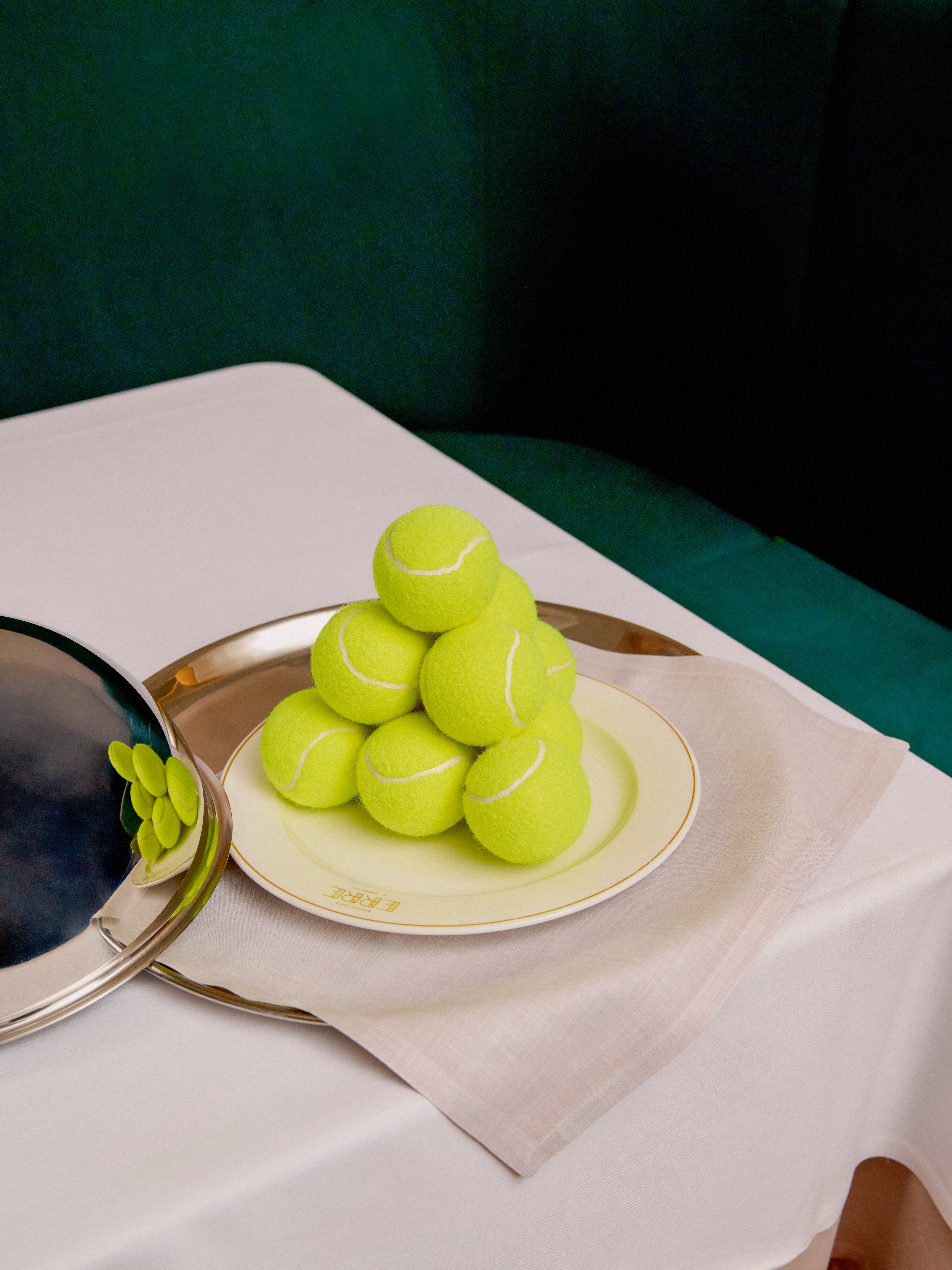 Pyramid of vibrant tennis balls on a luxury plate with silver cloche and tray.