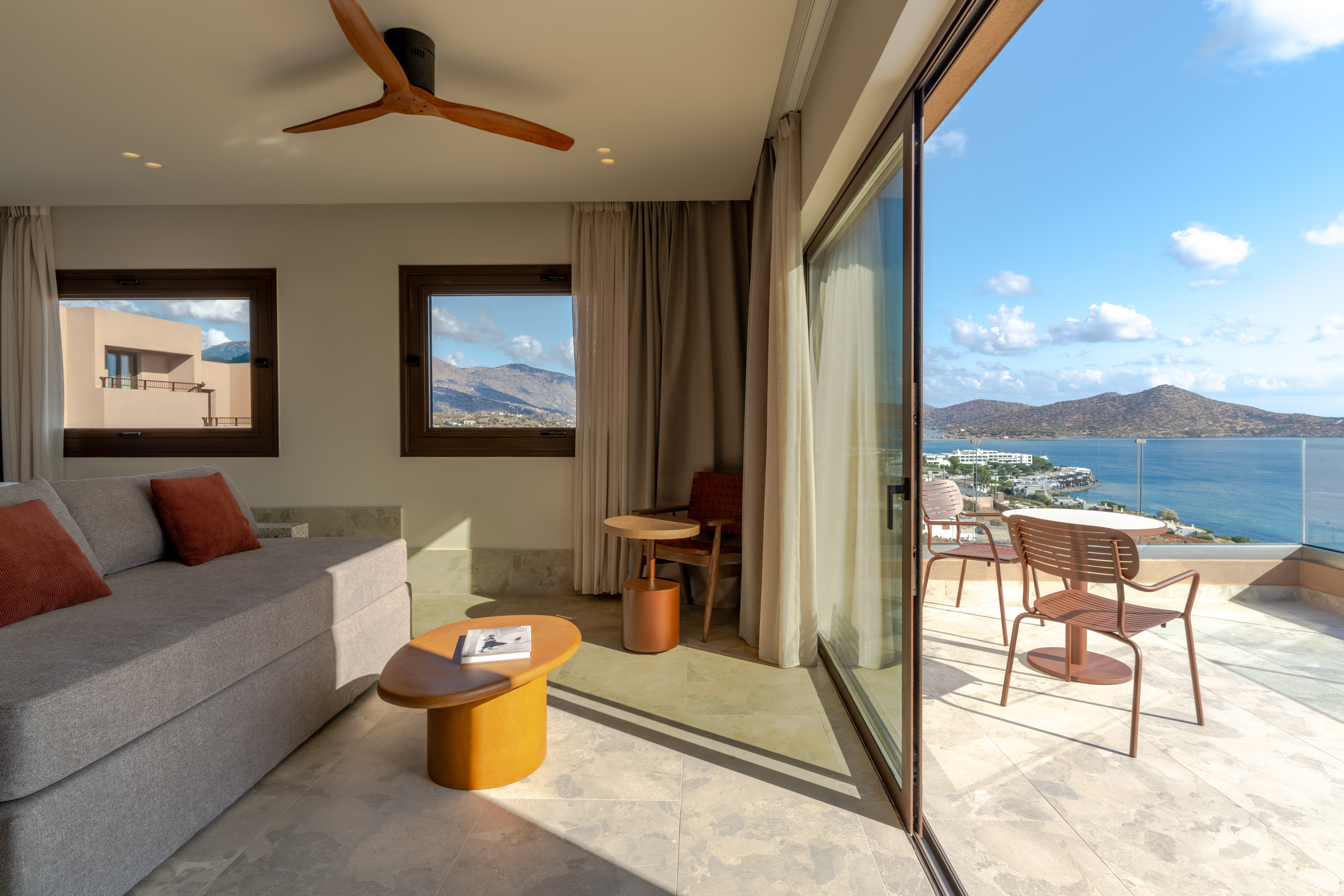 Modern luxury room with sea view balcony, sofa, and mountain landscape.