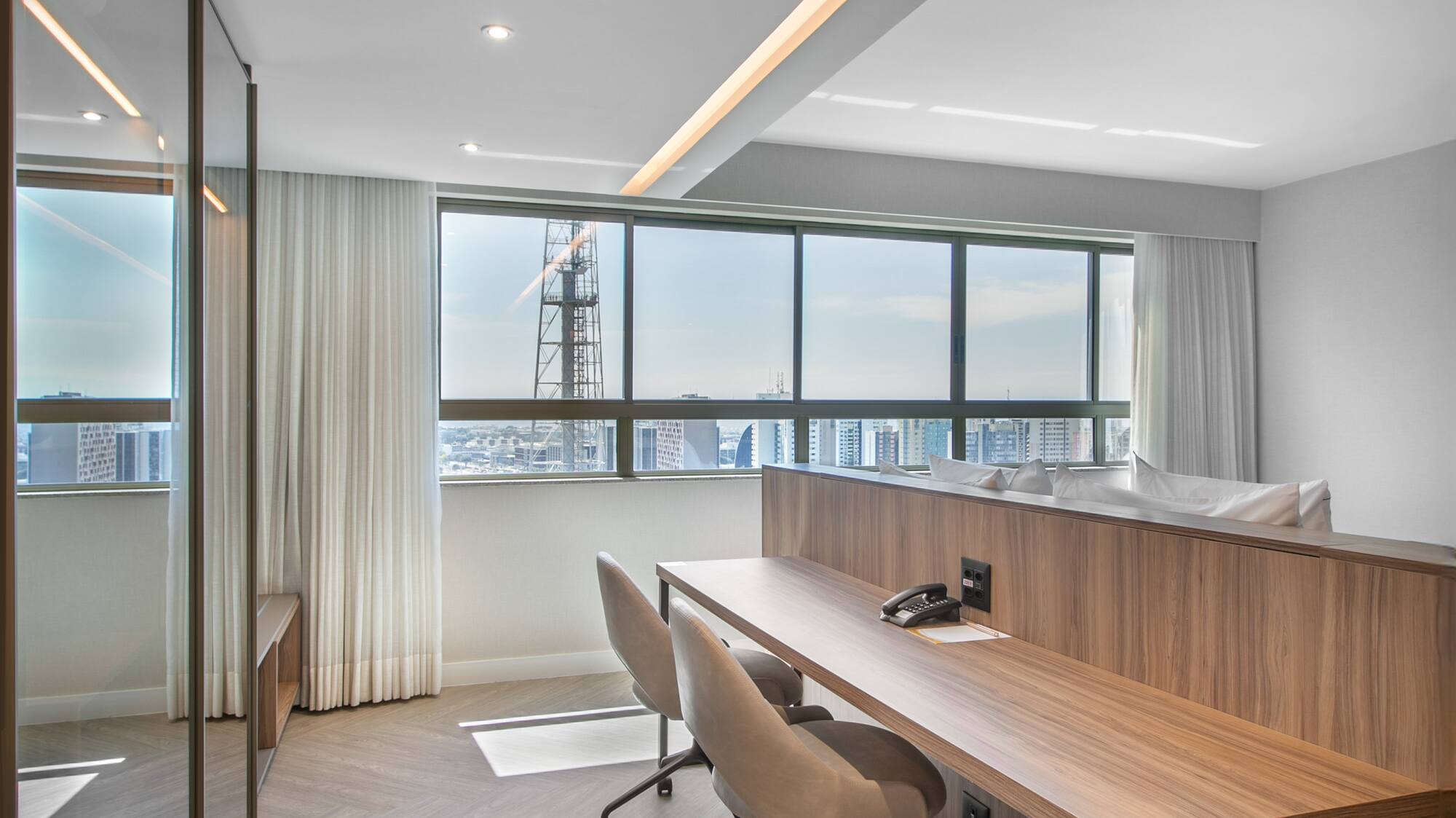 Modern hotel room workspace with city view, wooden desk, and two chairs.