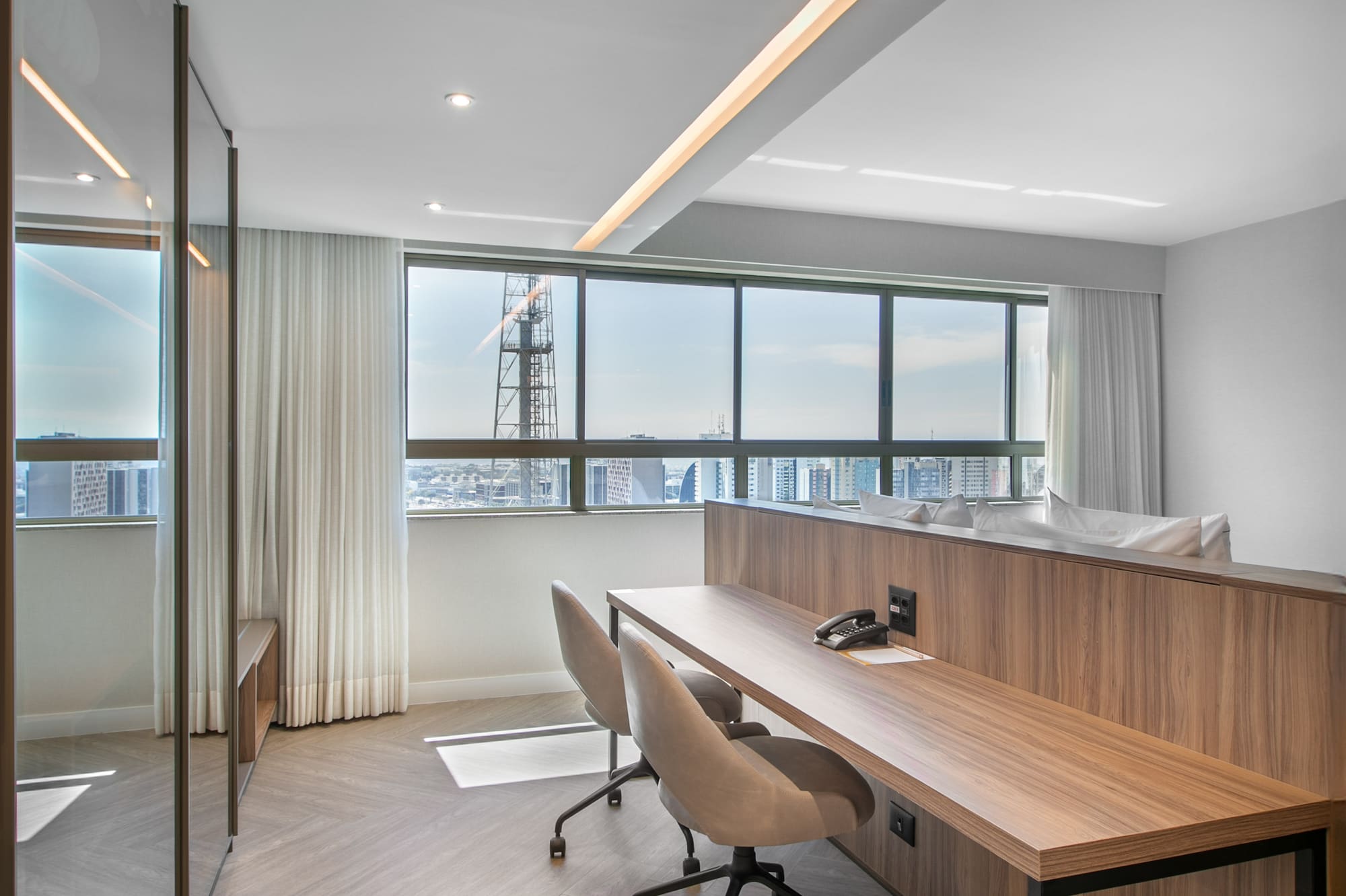 Contemporary workspace with wooden desk, two chairs, herringbone floor, city view.