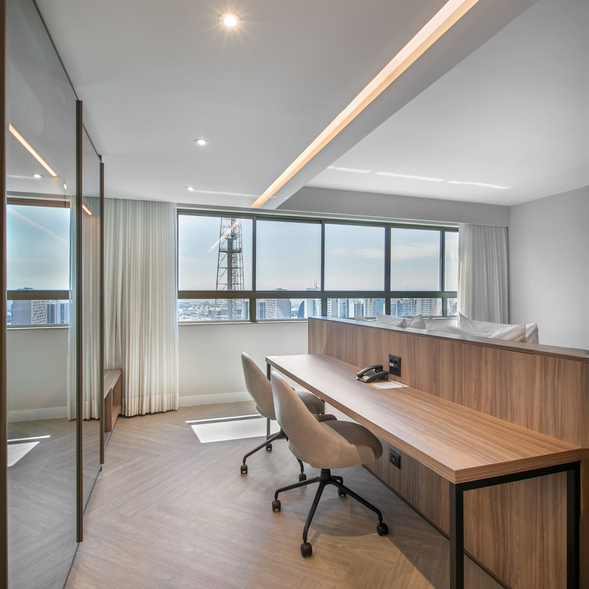 Contemporary workspace with wooden desk, two chairs, herringbone floor, city view.