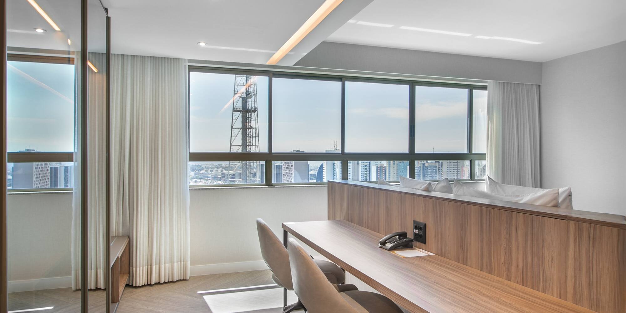 Modern hotel room workspace with city view, wooden desk, and two chairs.