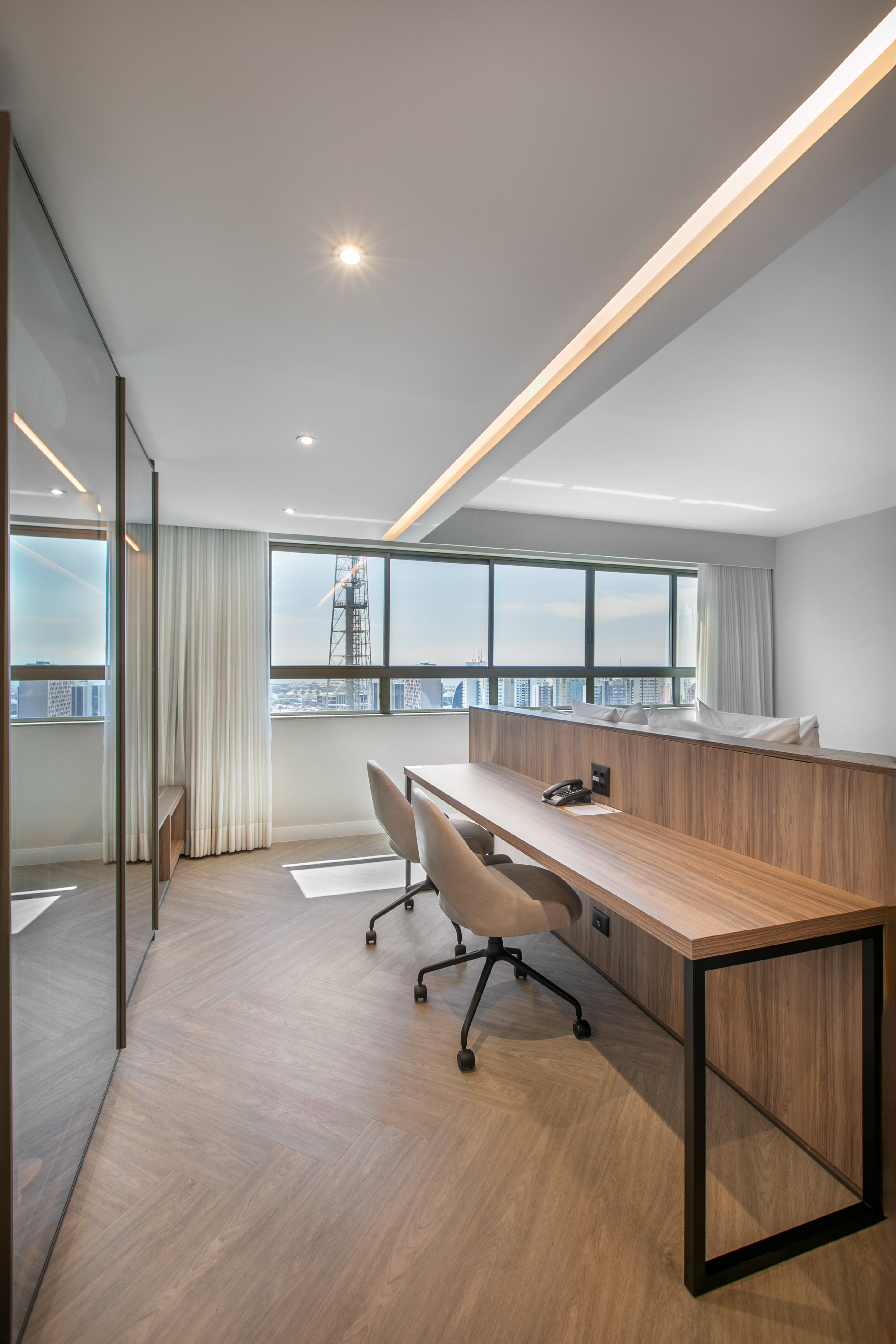 Contemporary workspace with wooden desk, two chairs, herringbone floor, city view.