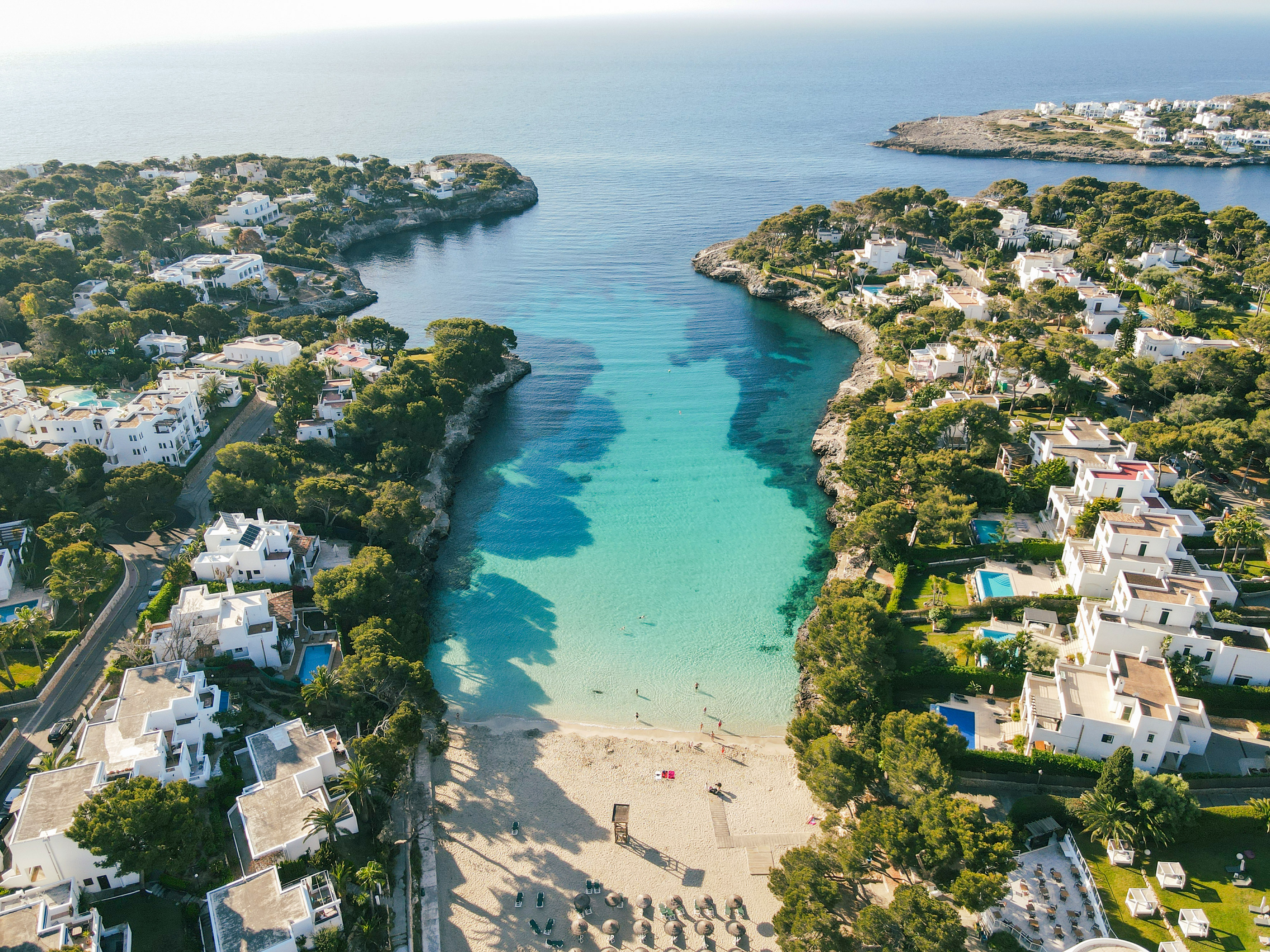 Aerial view: Mediterranean cove, turquoise water, sandy beach, white villas.
