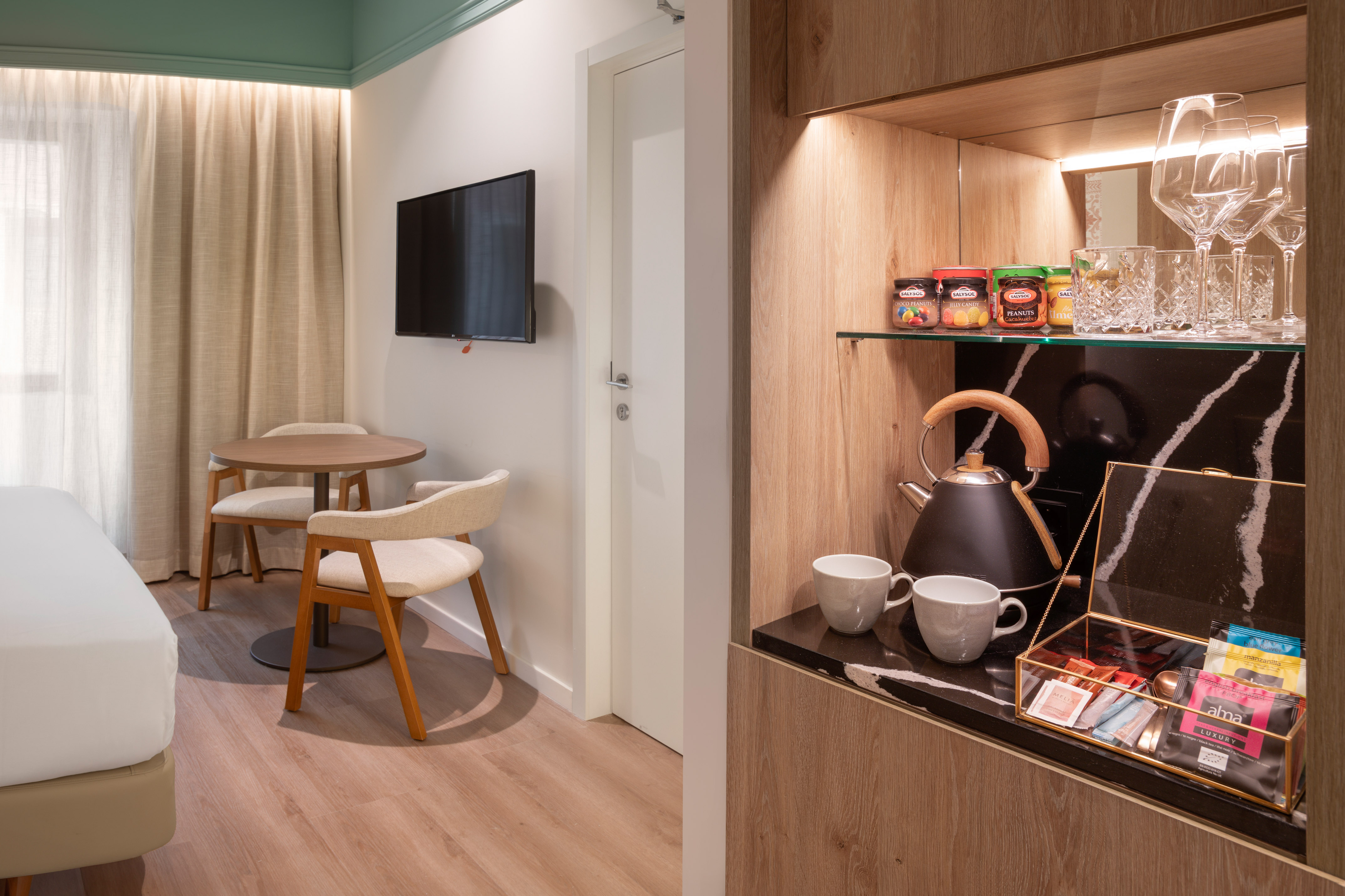 Modern hotel room interior with minibar, coffee station, TV, and dining area.