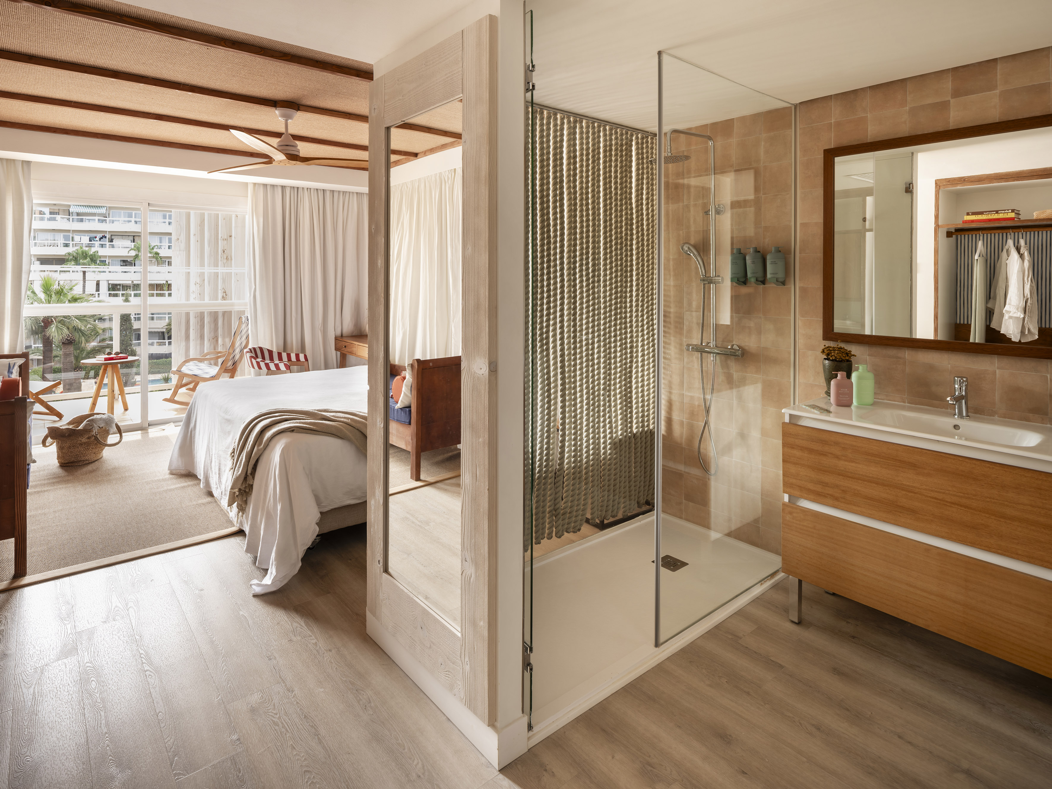 Modern hotel room with bed, balcony view, and glass walk-in shower.