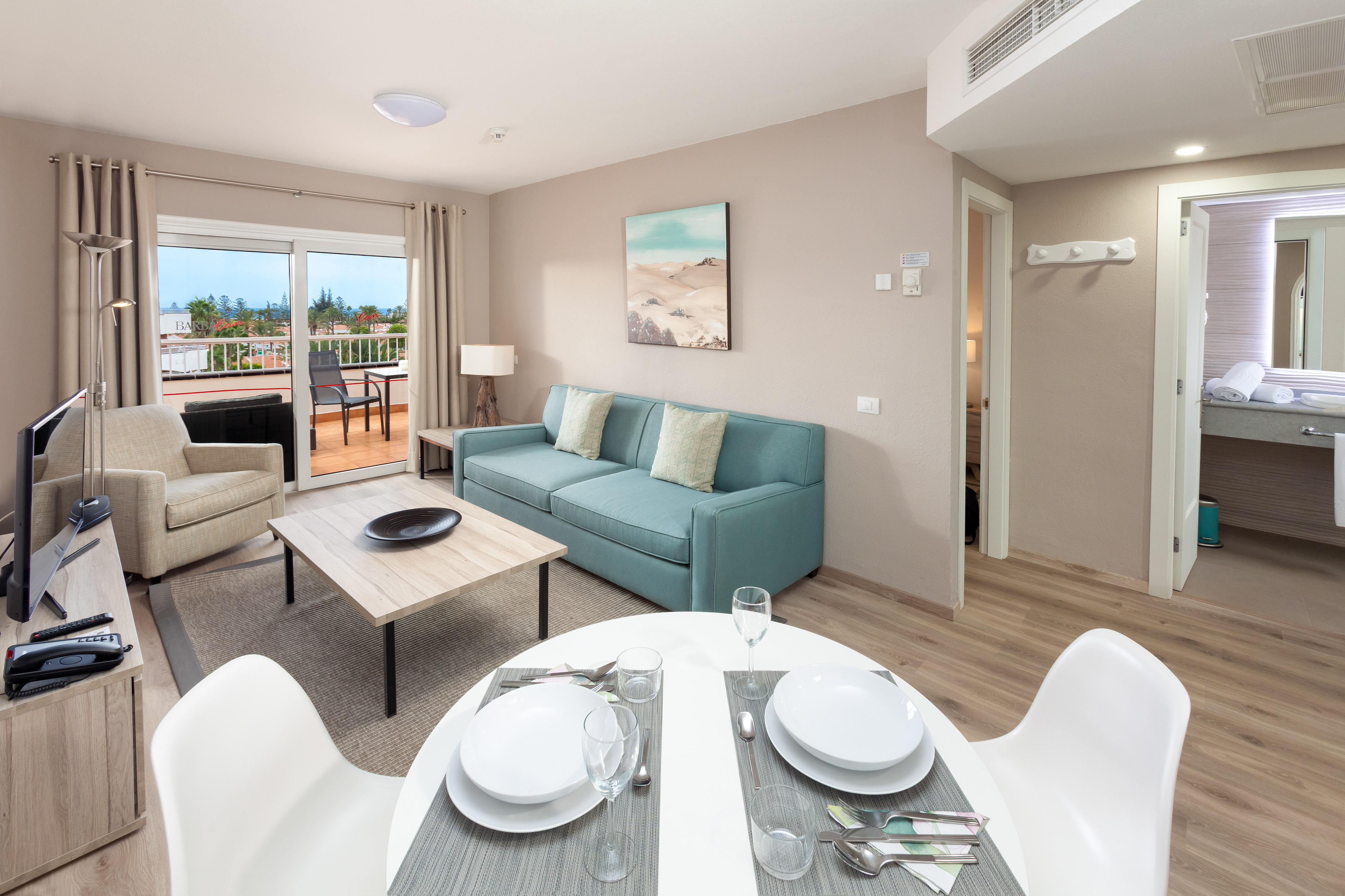 Modern apartment living room with teal sofa, dining area, and balcony ocean view.