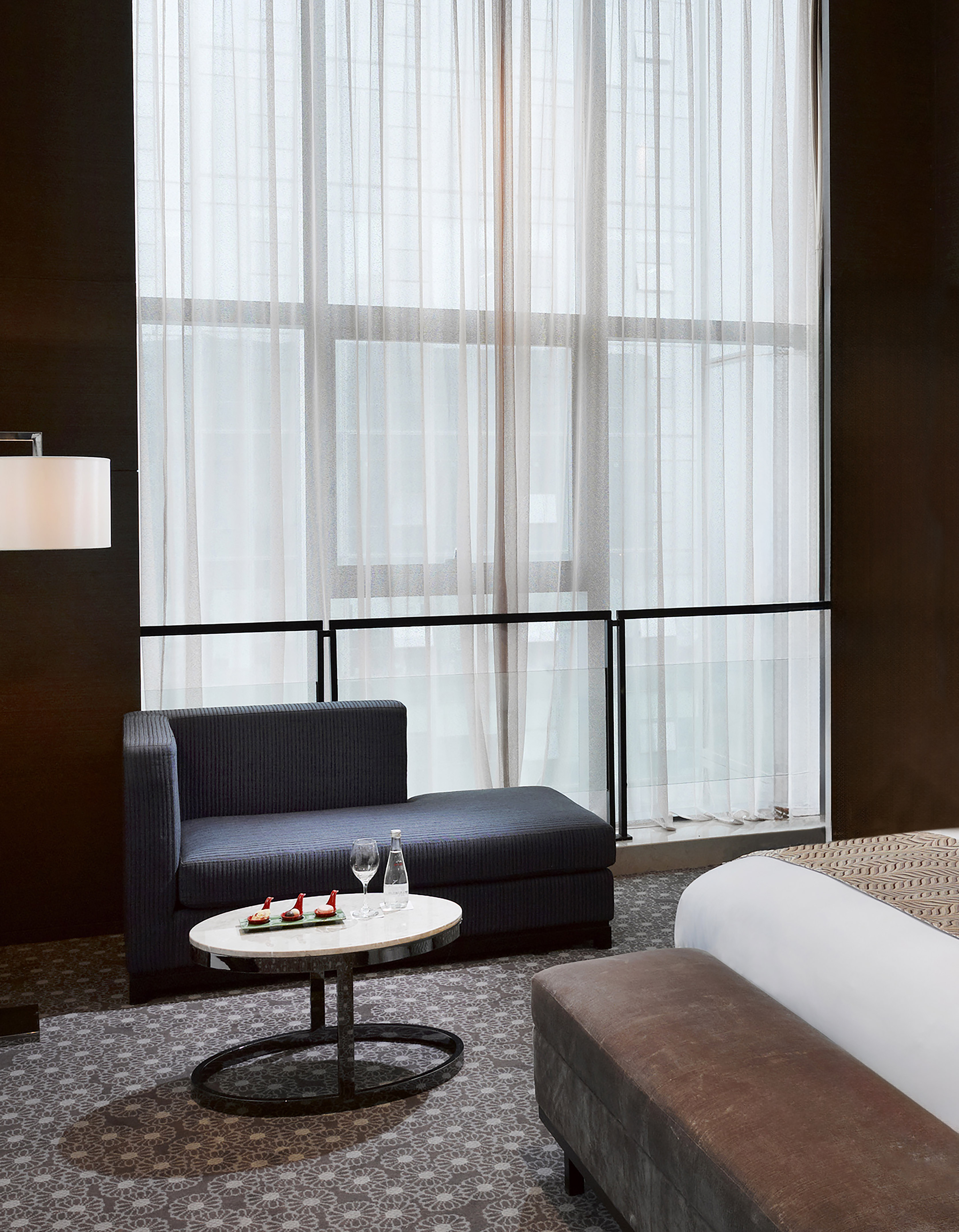 Modern hotel lounge with sheer curtains, dark chaise, coffee table, appetizers.