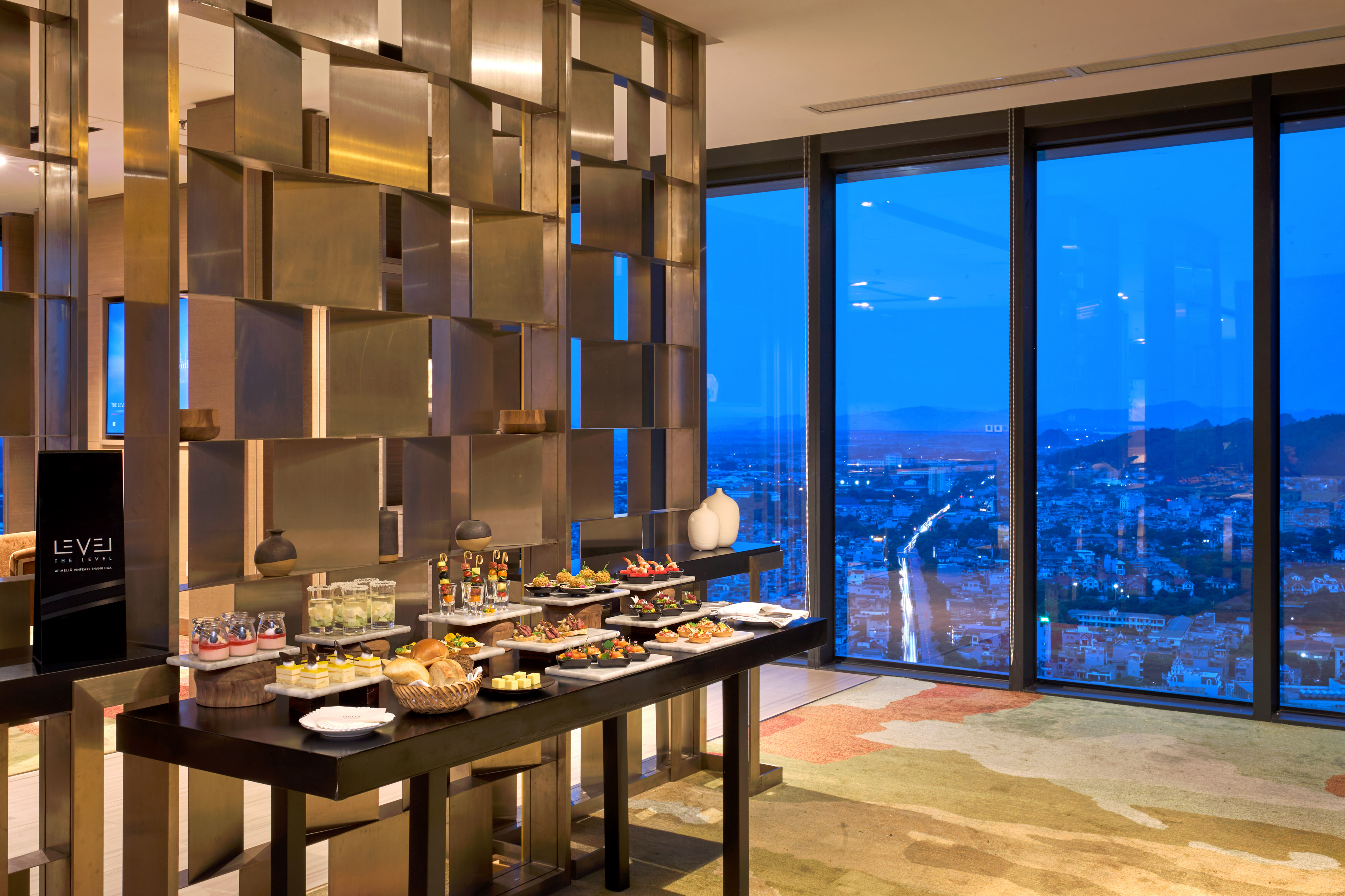 Modern lounge buffet with appetizers and panoramic city view at night.