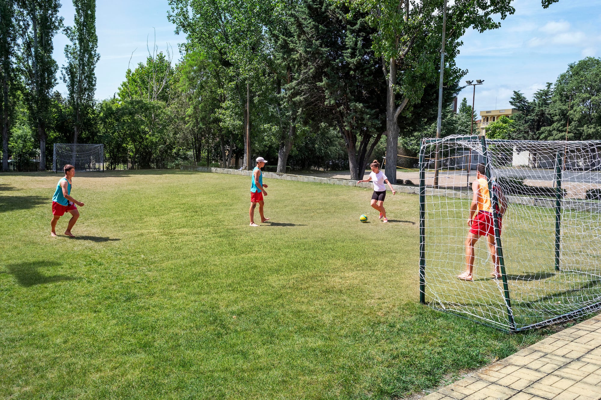 Four youth playing soccer on a sunny green field with two goals.