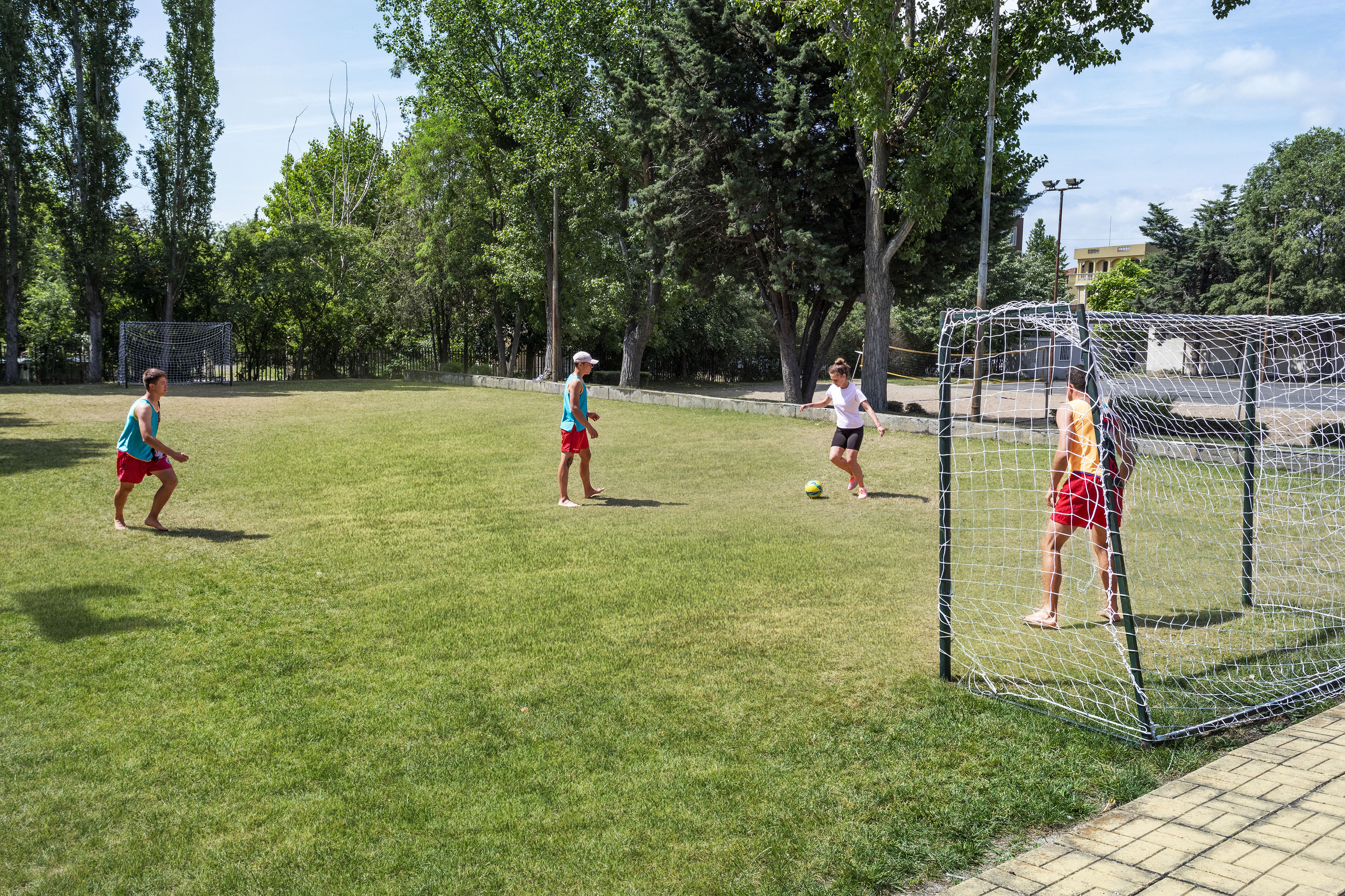 Four youth playing soccer on a sunny green field with two goals.