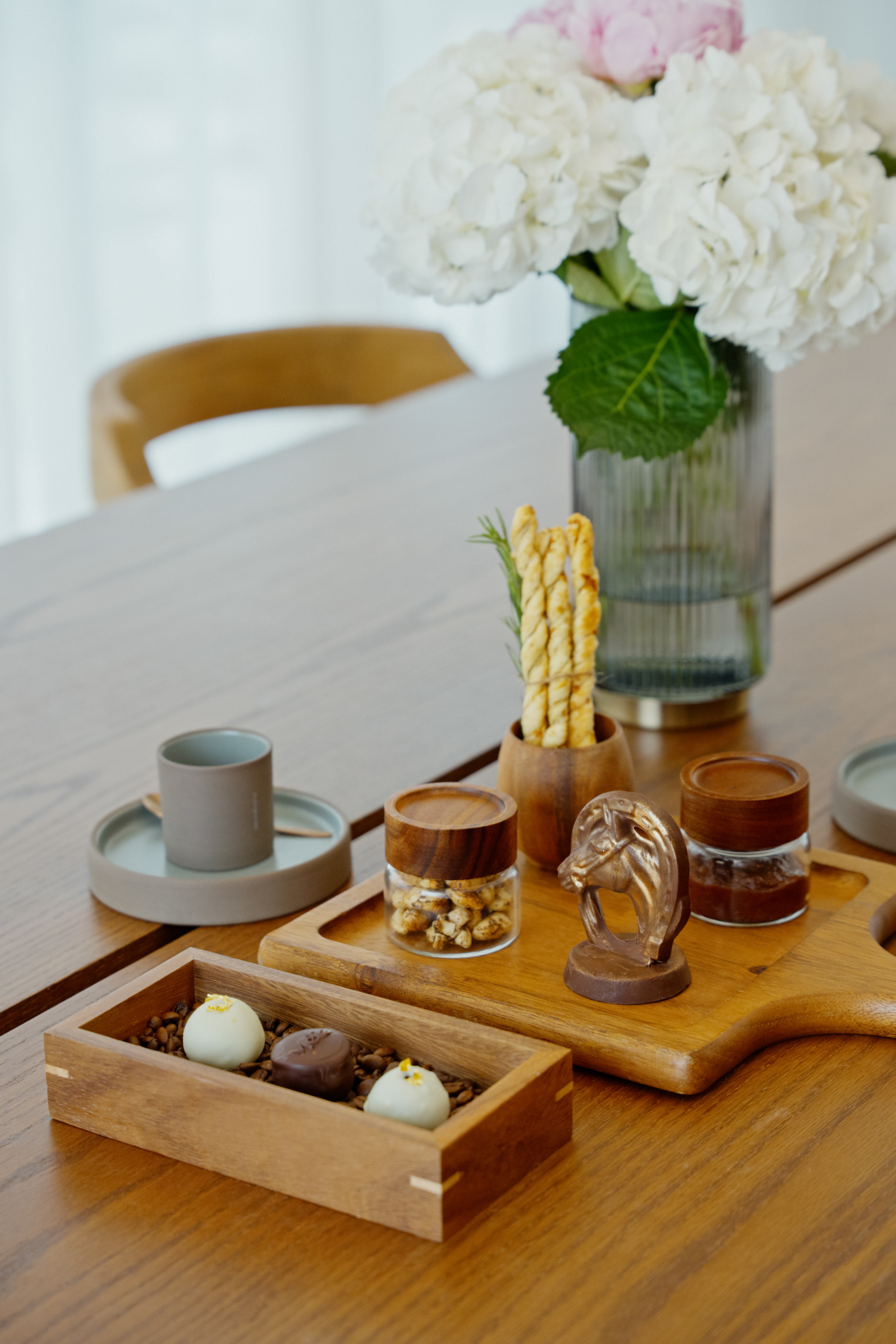 Gourmet chocolates, snacks, breadsticks, and white hydrangeas on wooden table.