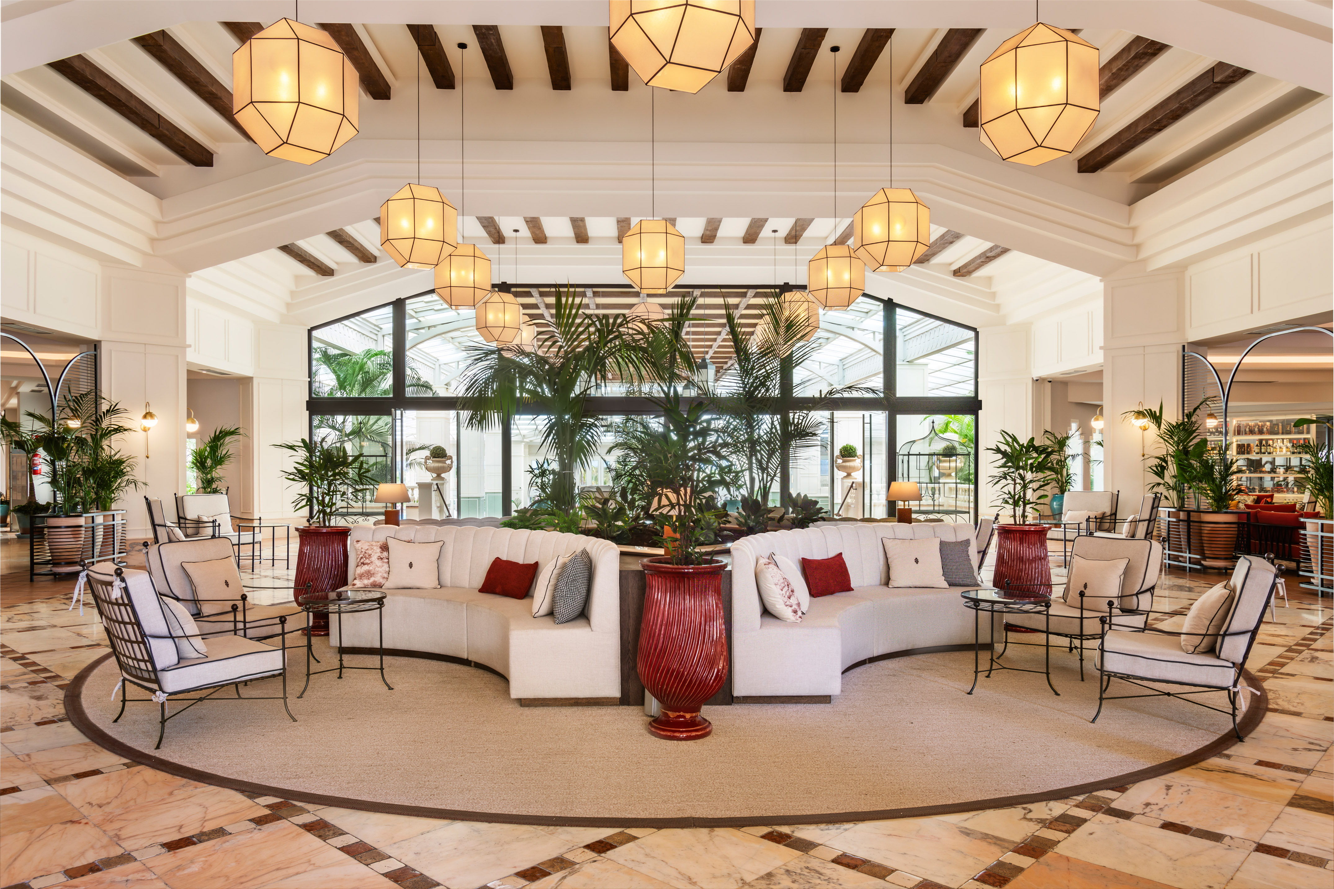Elegant hotel lobby with curved sofas, geometric lights, and lush tropical plants.