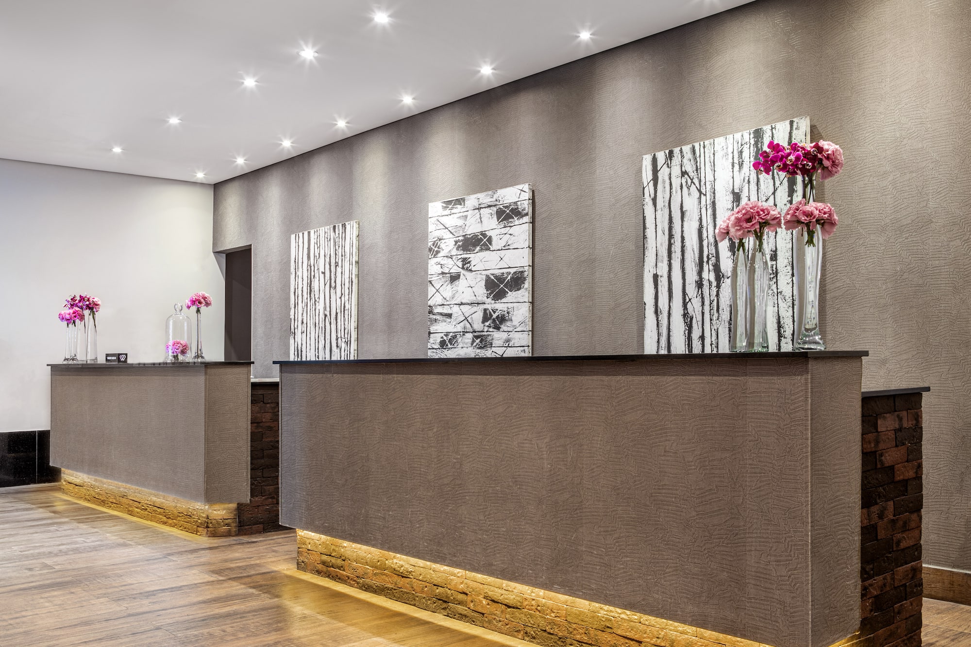 Modern hotel reception area with two stylish desks, pink flowers, and abstract art.