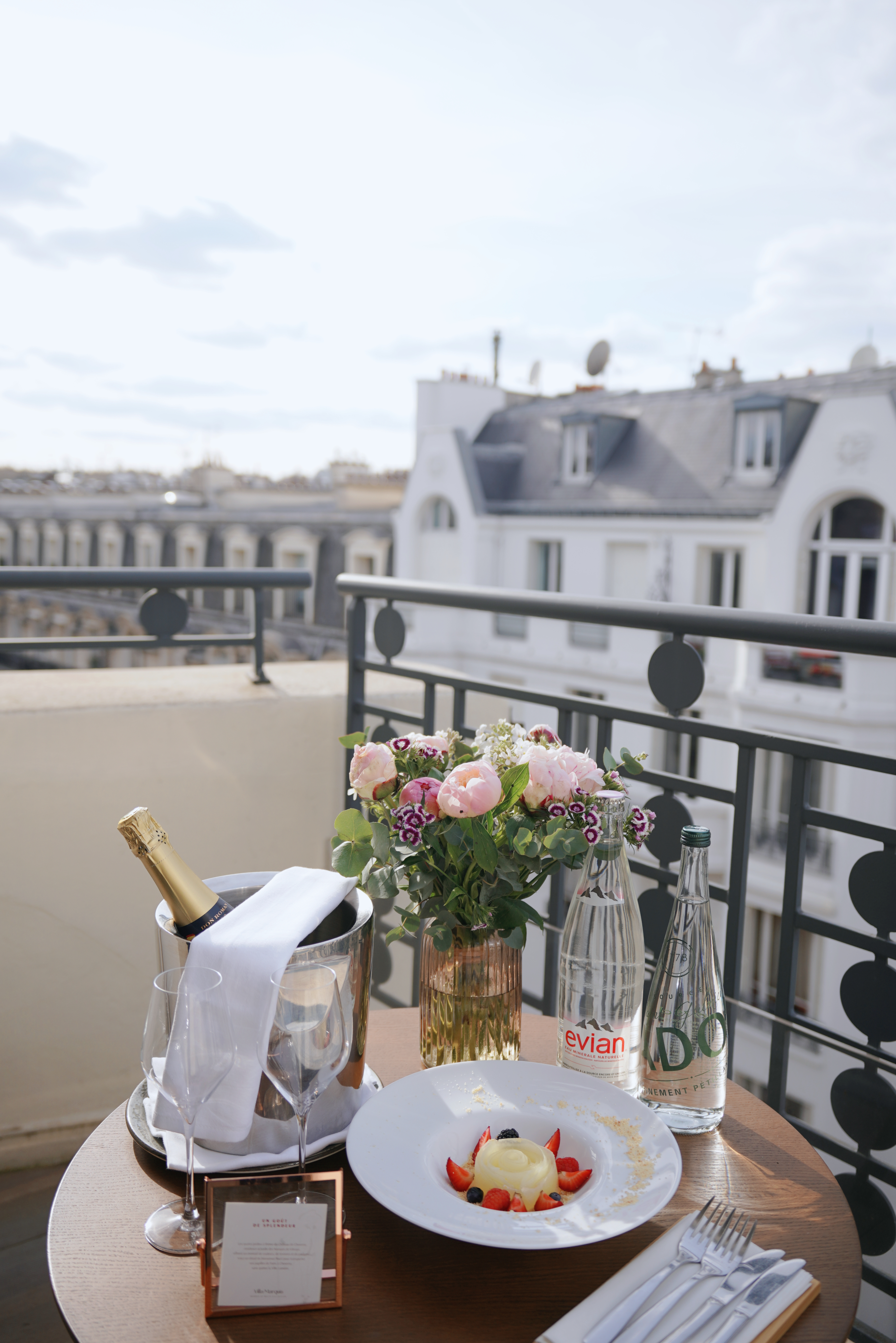 a table with a plate of champagne and flowers on a balcony