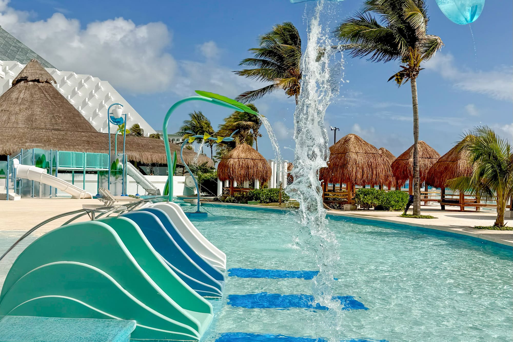 Tropical water park with colorful slides, water features, palm trees, and resort.