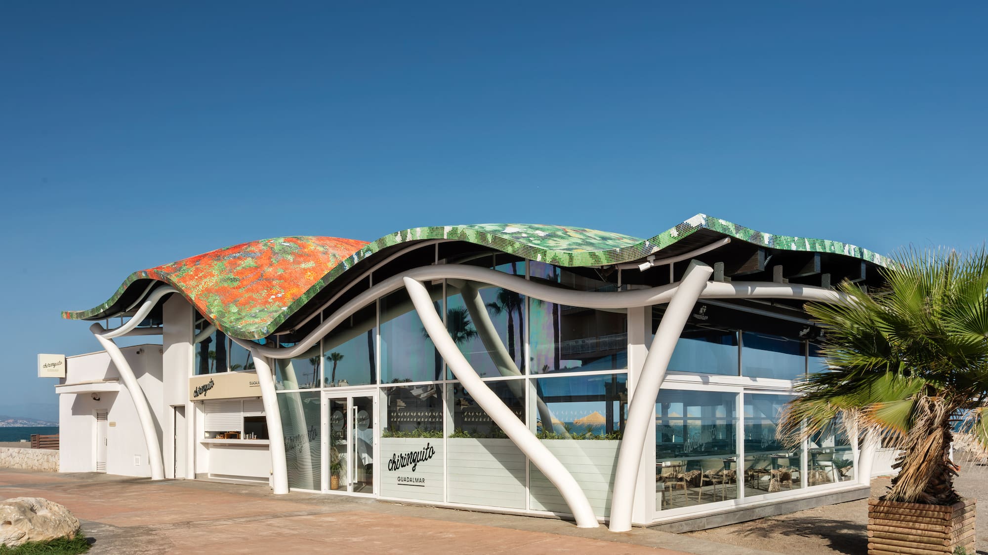 Chiringuito Guadalmar with colorful wavy roof, modern beachfront design.