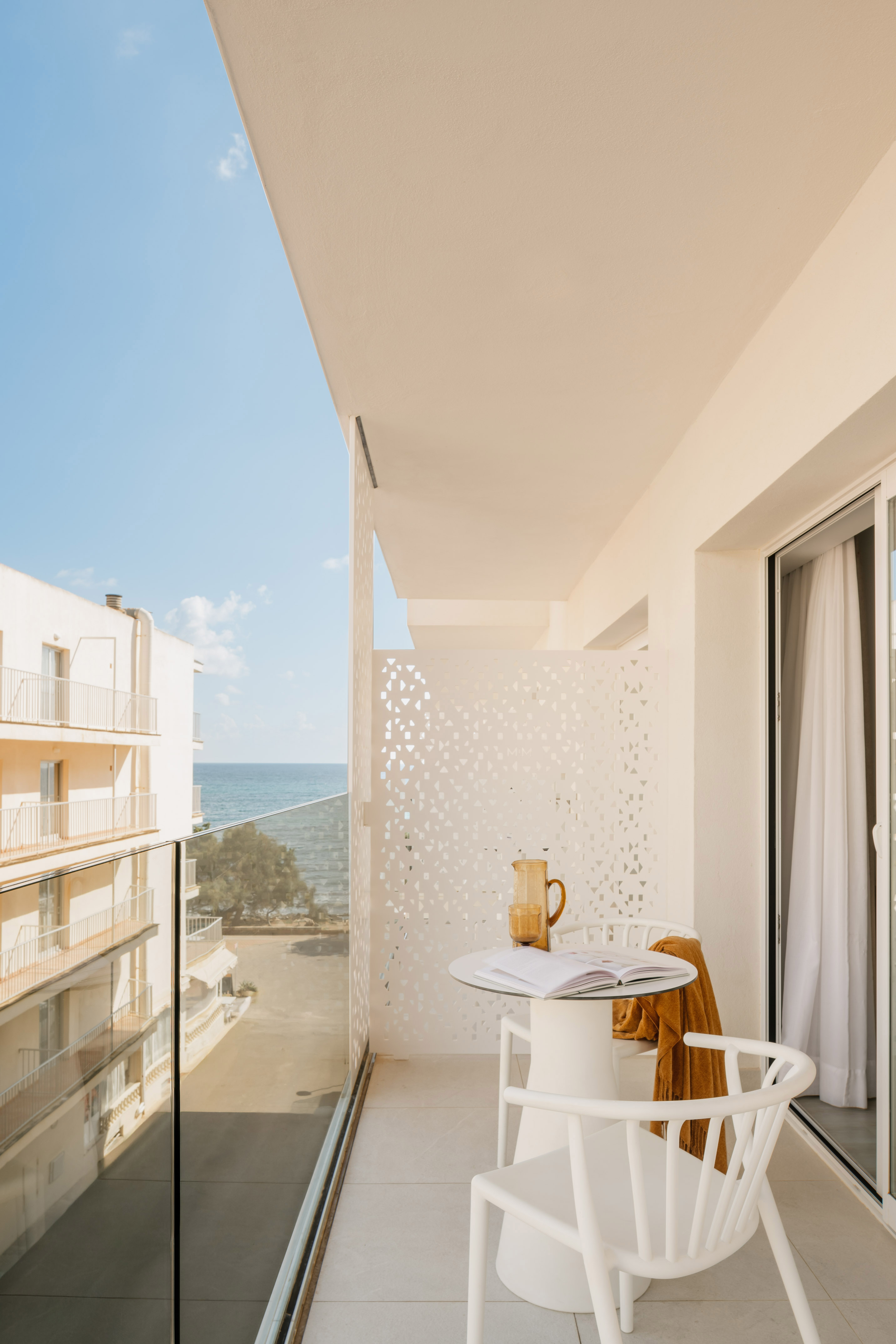 Coastal hotel balcony with white furniture, open book, and stunning ocean view.